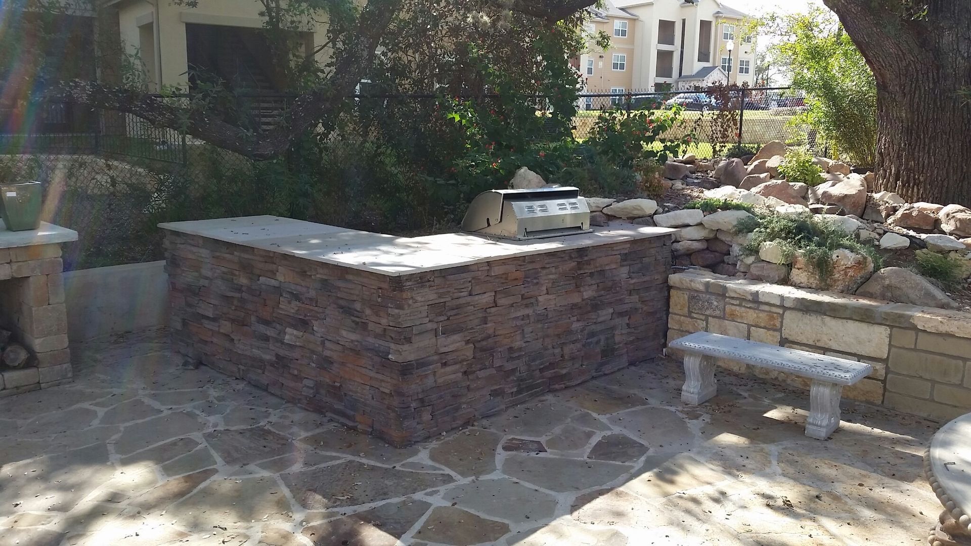 A stone patio with a grill and a bench