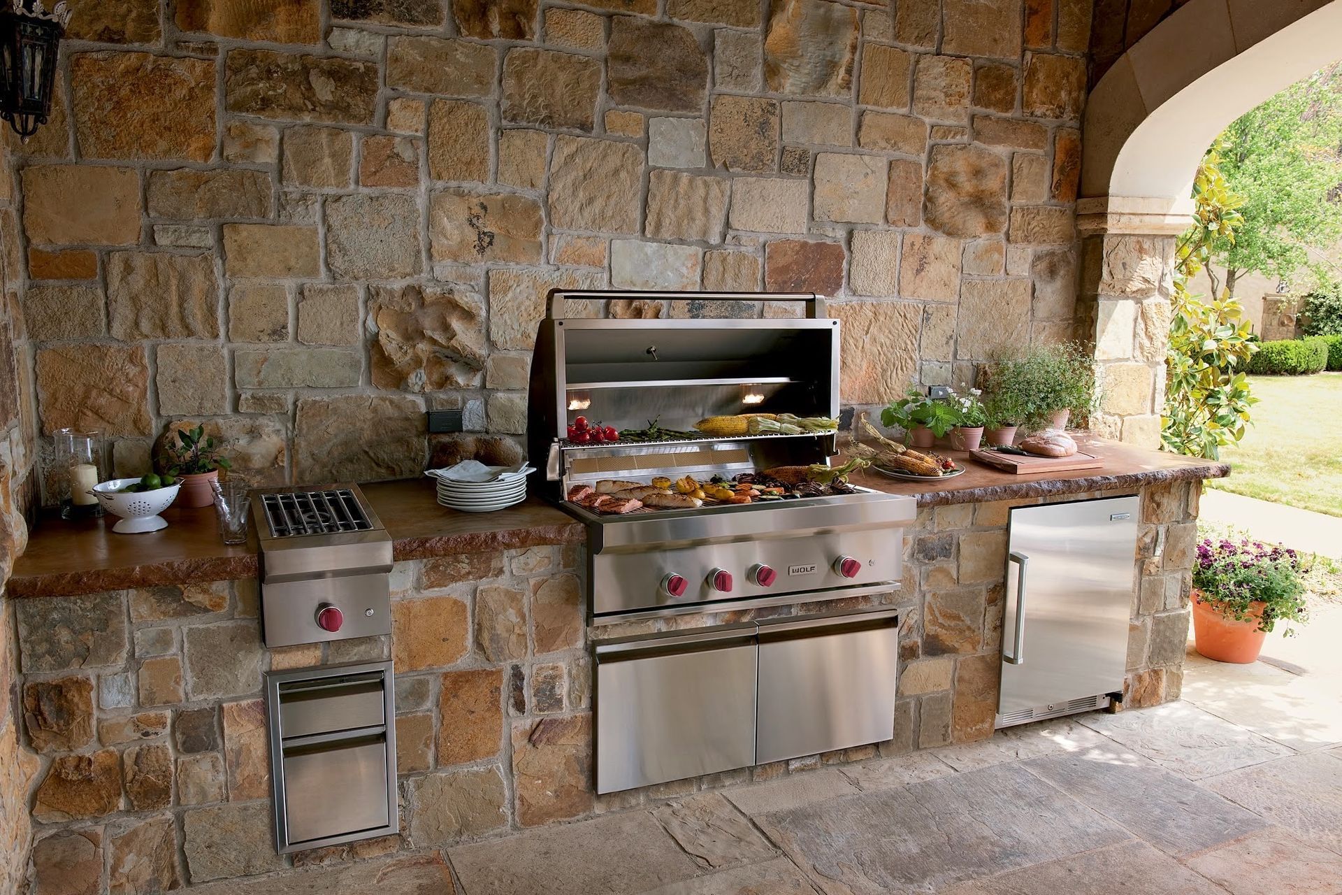 An outdoor kitchen with stainless steel appliances and a stone wall