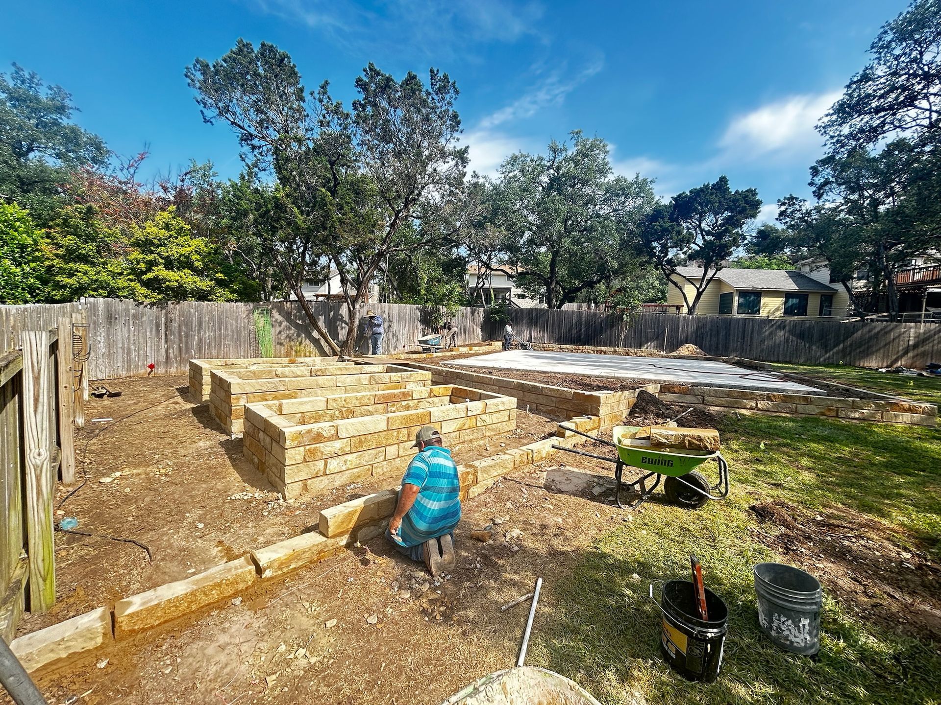 A man is working on a brick wall in a backyard.