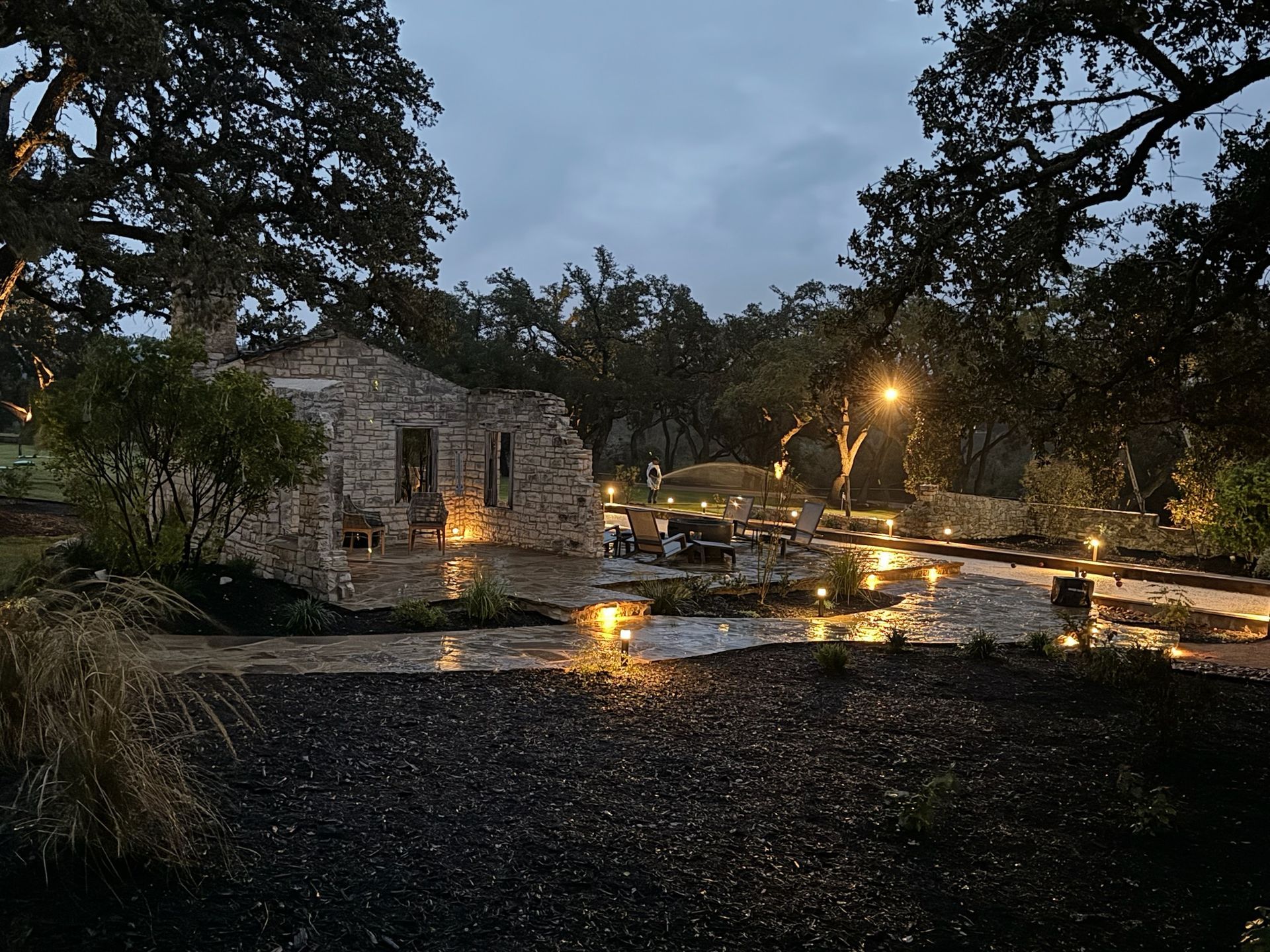 A stone house is surrounded by trees and lights at night.