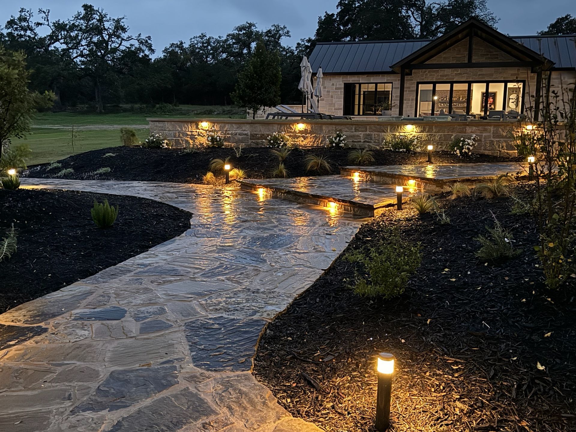 A stone walkway leading to a house is lit up at night.