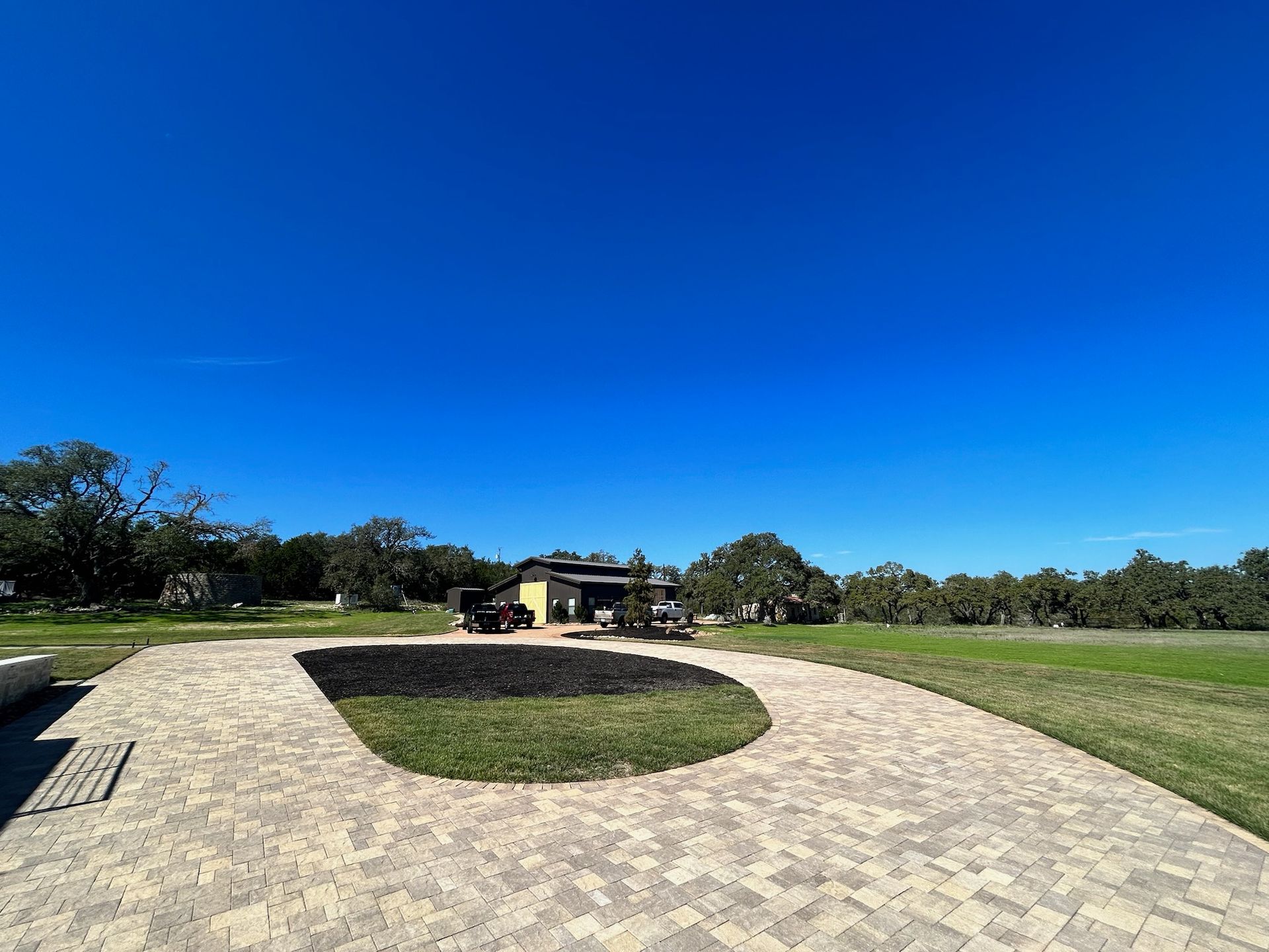 A brick driveway leading to a house in the middle of a grassy field.