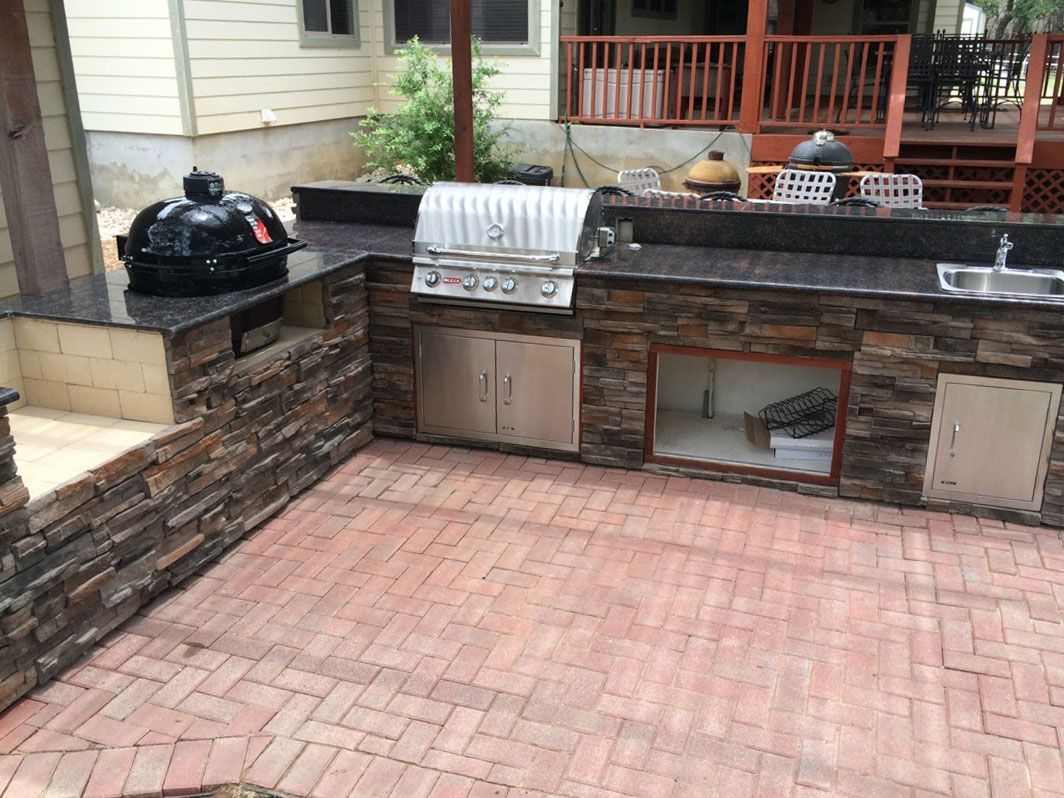 An outdoor kitchen with a grill , sink , and brick floor.