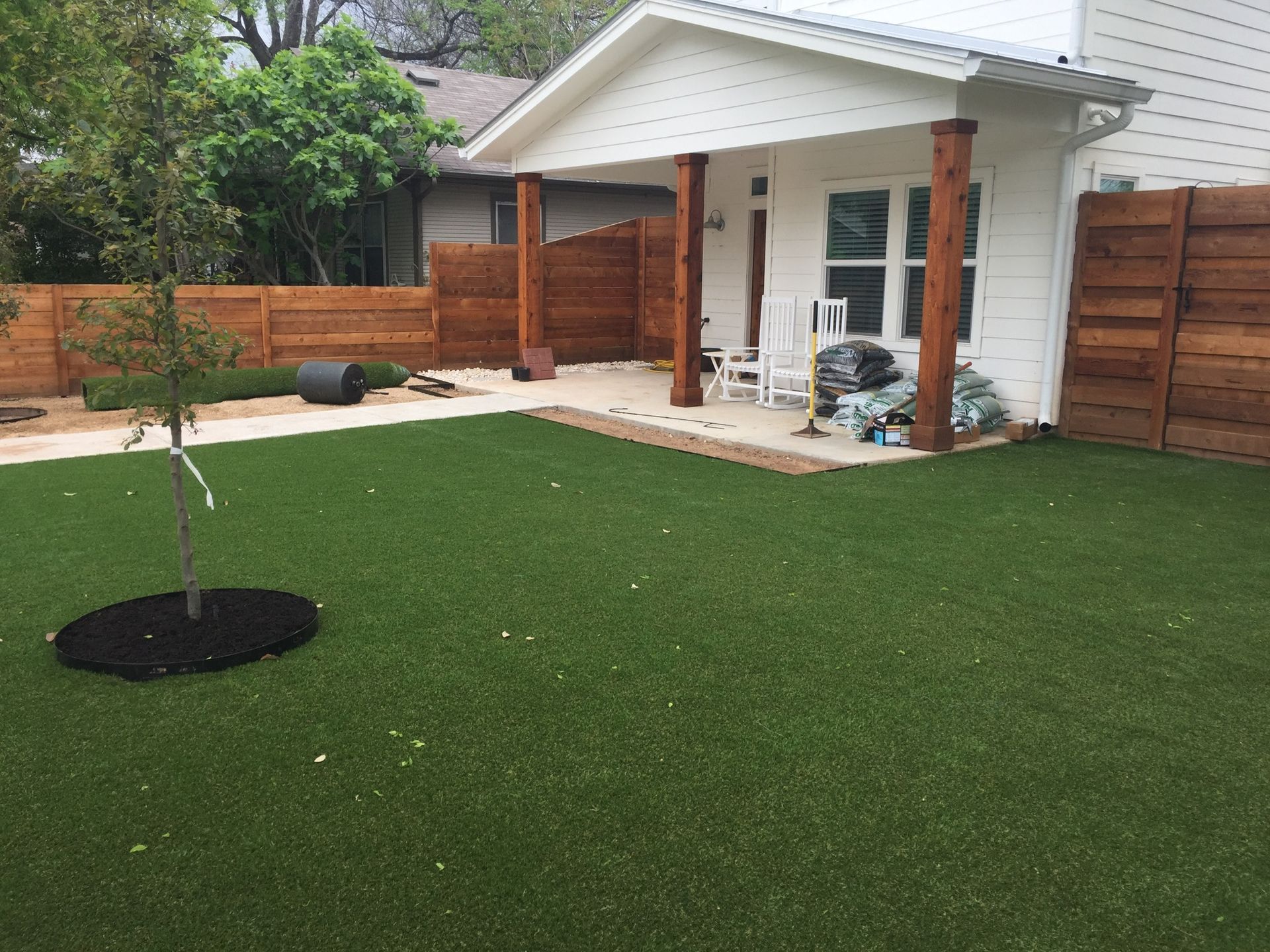 There is a tree in the middle of the grass in the backyard of a house.