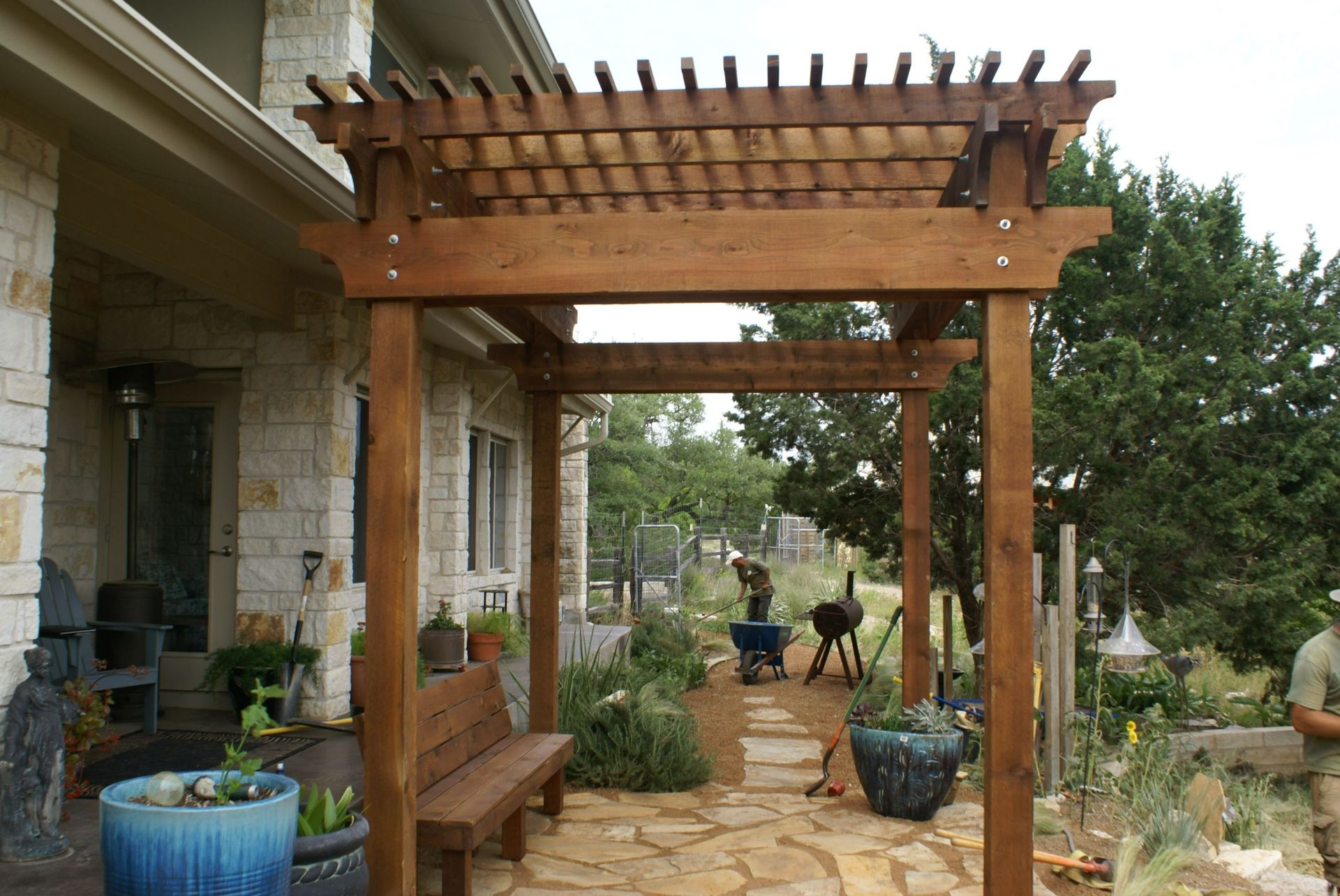 A wooden pergola is in front of a stone house