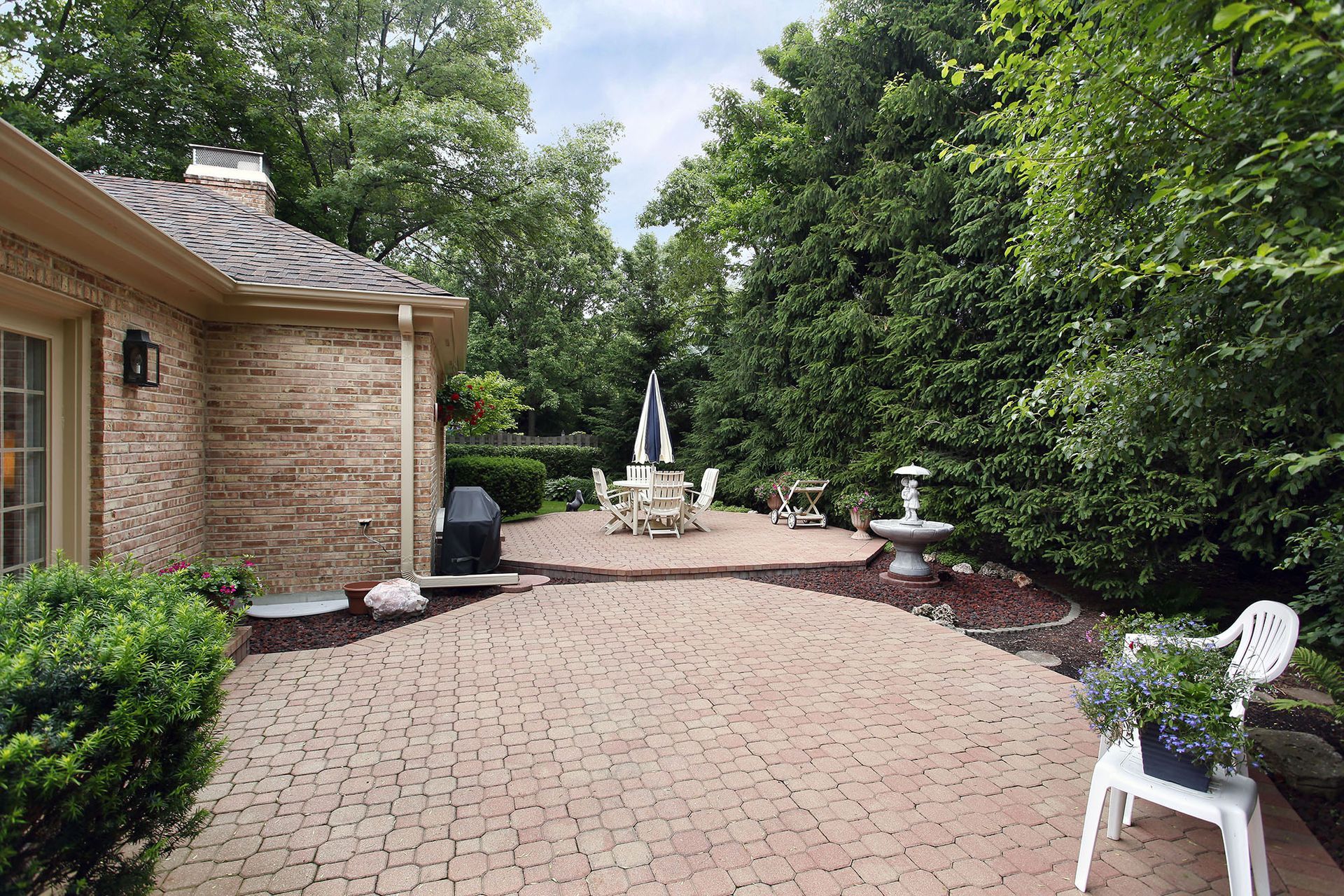 A brick patio with a table and chairs and a fountain in the backyard of a house.