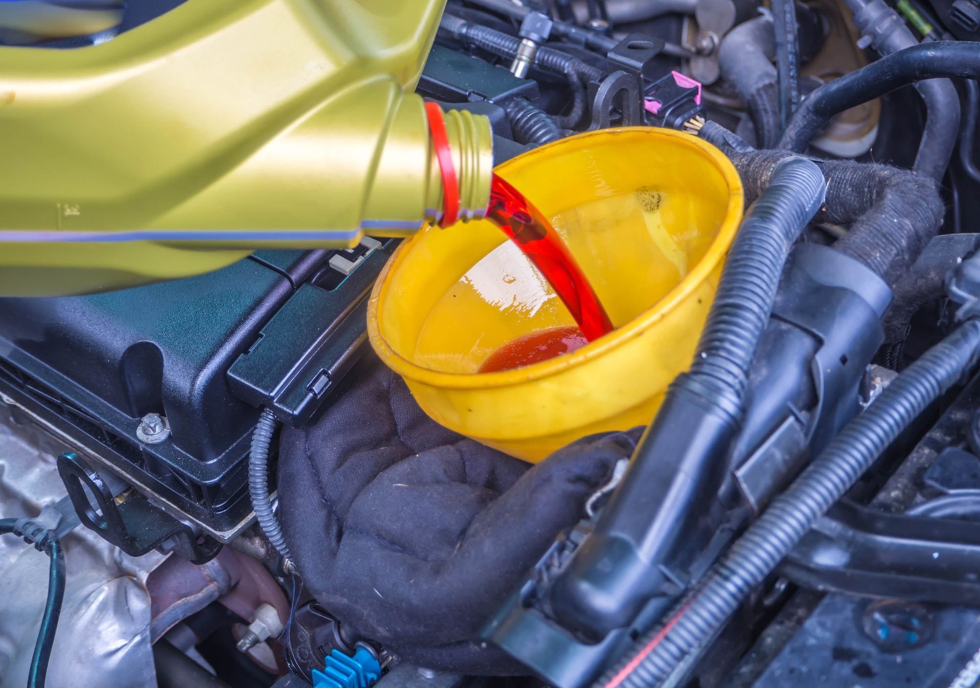 Red motor oil pouring from a bottle into a yellow funnel in a car engine bay