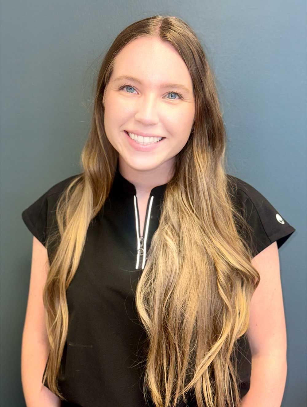 A woman with long hair is wearing a black shirt and smiling.