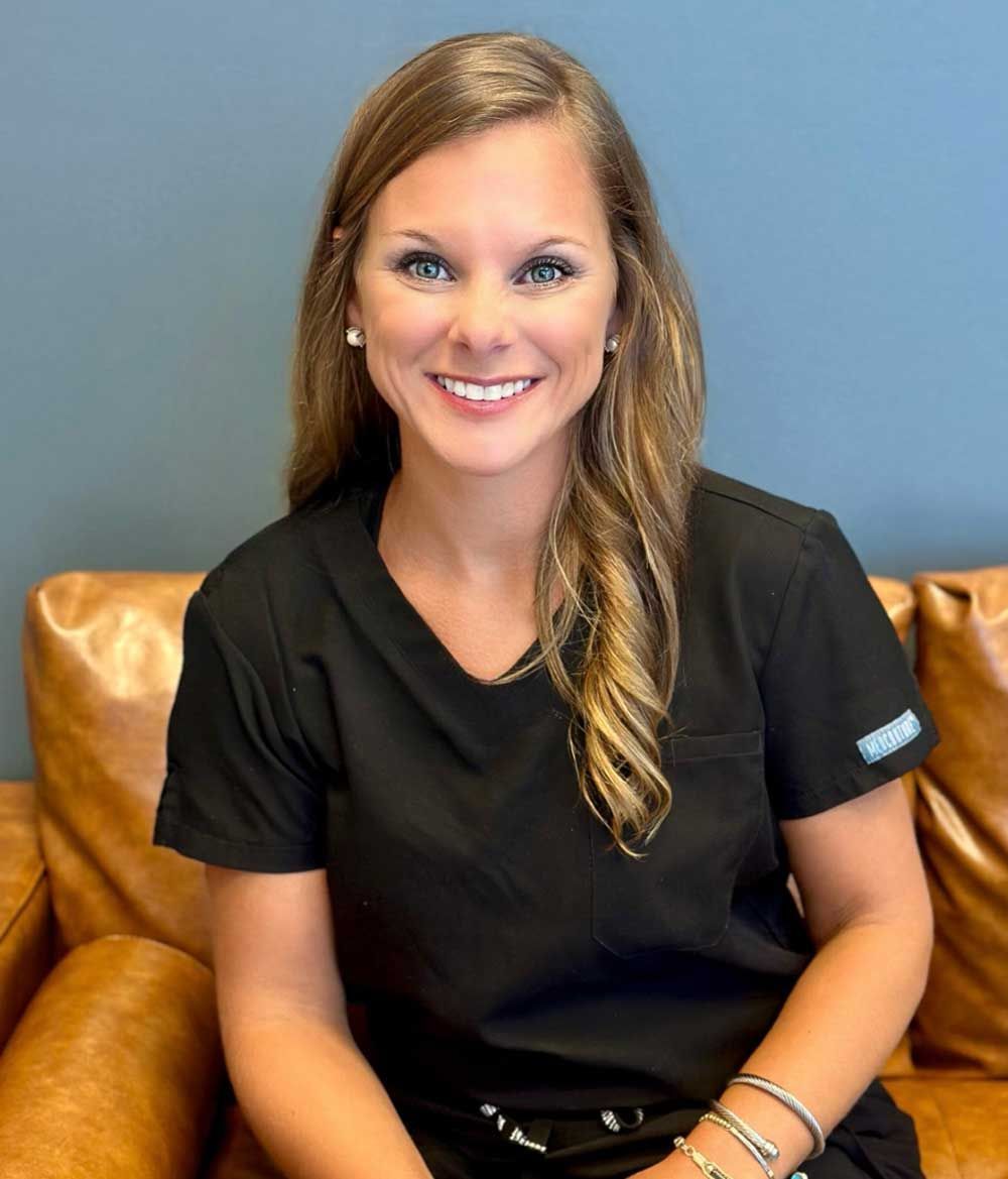 A woman in a black shirt is sitting on a couch and smiling.