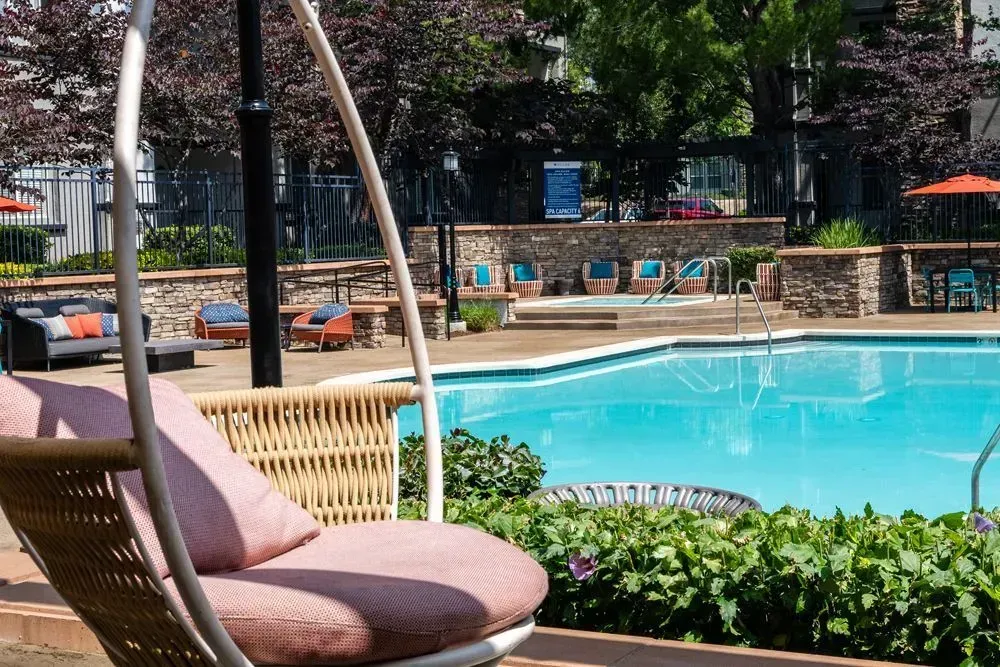 Poolside lounge chair beside a turquoise swimming pool with trees and umbrellas in the background