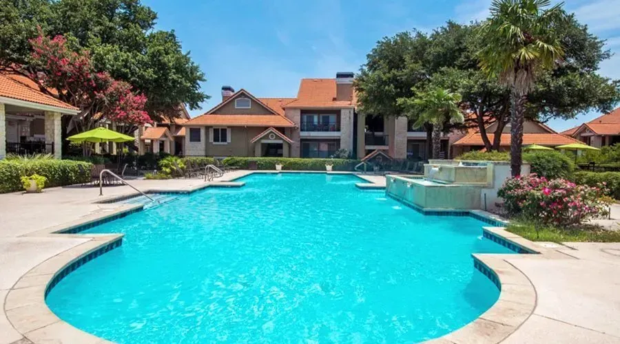 Sunny resort-style pool with turquoise water, lounge chairs, and a house in the background