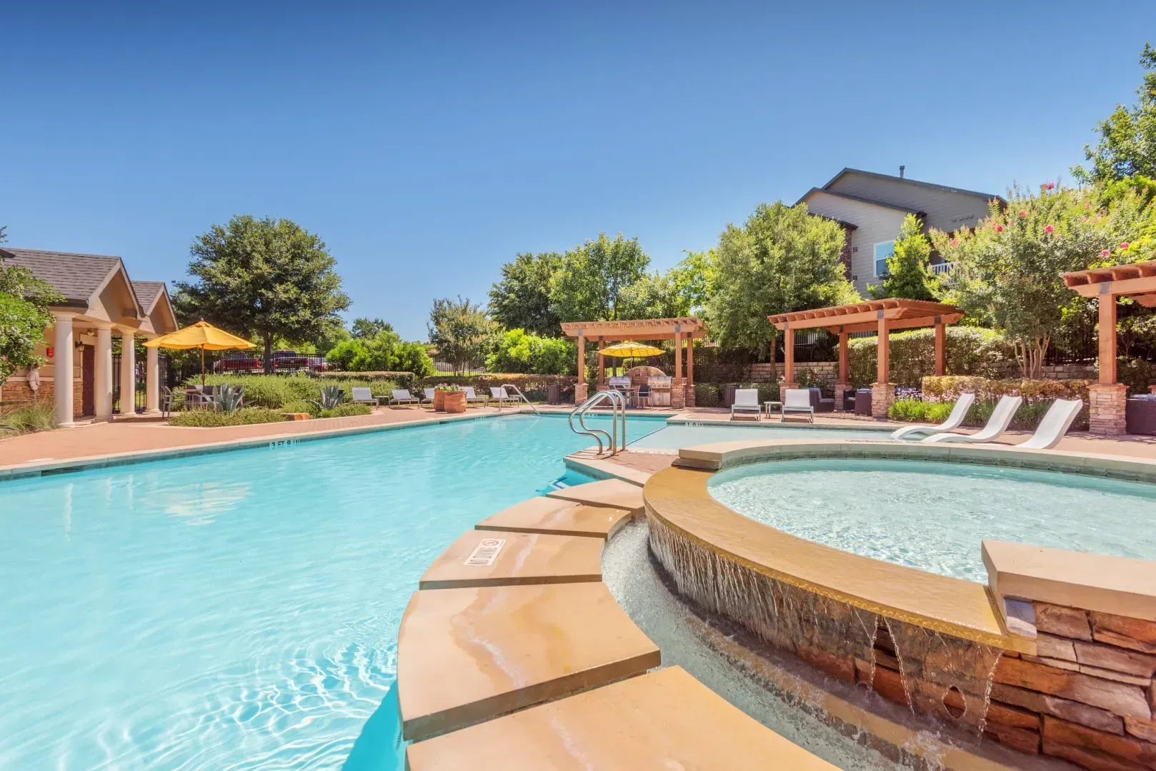 Resort pool with turquoise water, hot tub, lounge chairs, and pergolas under a clear blue sky