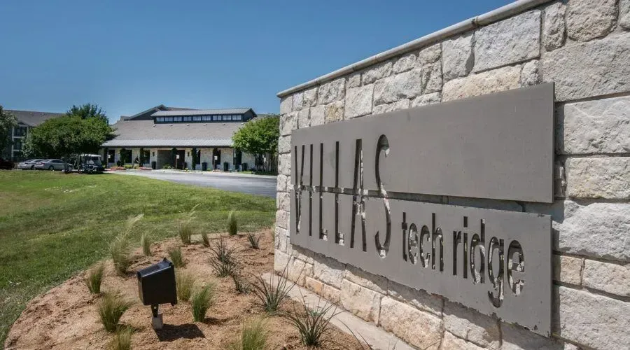 Mild steel tech ridge sign beside a stone wall, with a modern campus building in the background