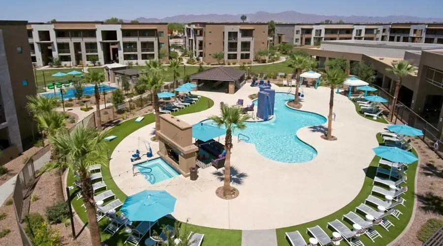 Resort-style pool courtyard with palm trees, lounge chairs, and blue water under a sunny sky
