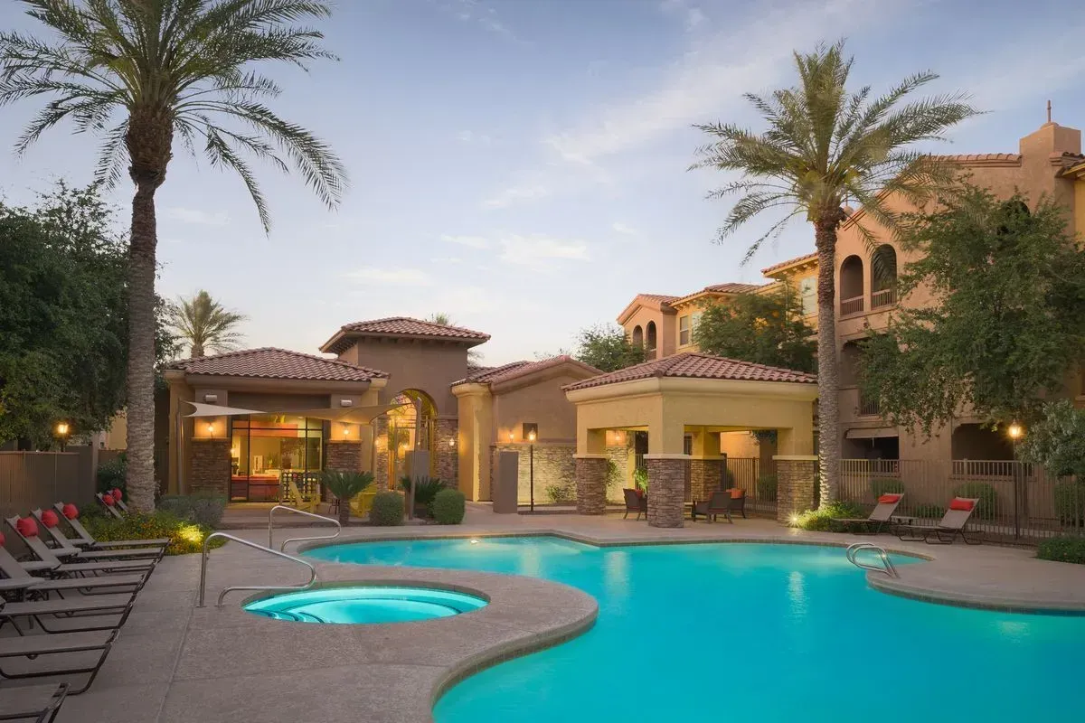 Luxury resort courtyard with turquoise pool, palm trees, lounge chairs, and a warm-lit villa at dusk