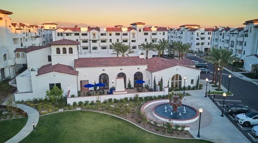 Courtyard of white resort buildings at sunset, with a fountain, lawn, and palm trees.