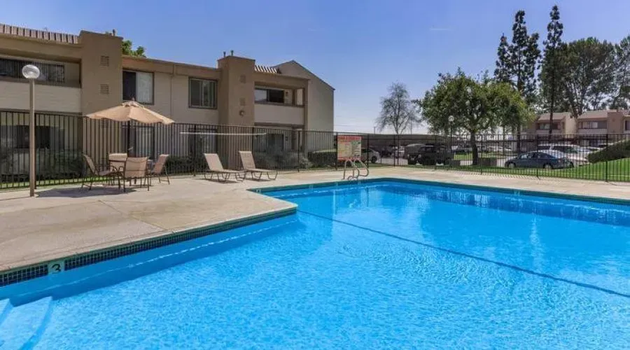 Apartment complex pool with blue water, lounge chairs, and shaded patio area.