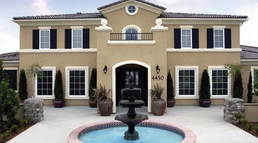 Two-story beige house with black shutters and a front fountain in a landscaped courtyard