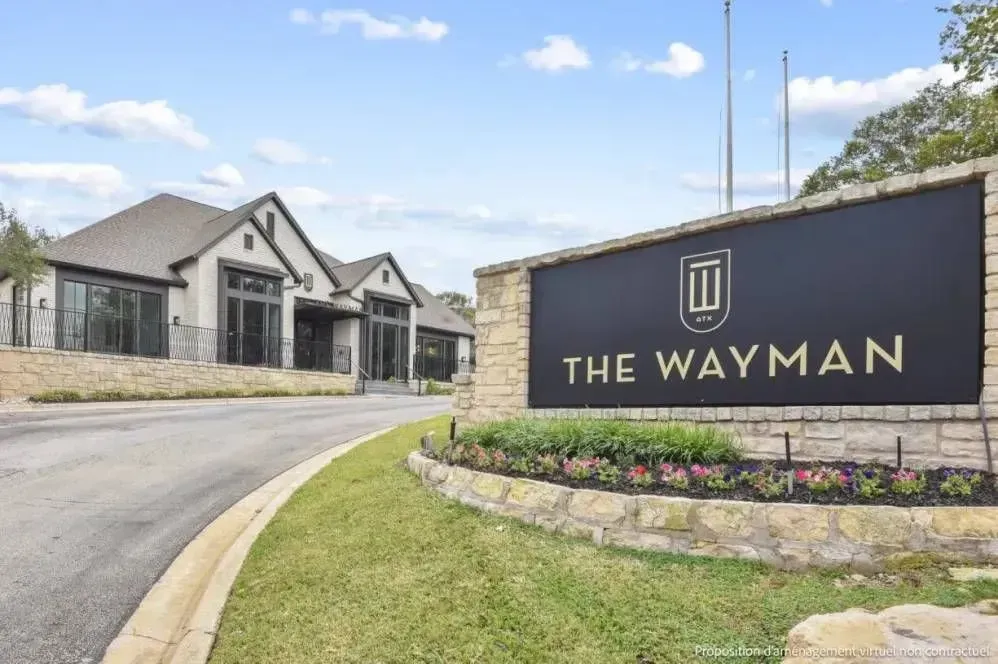 The Wayman entrance sign beside modern townhomes on a curved driveway under a blue sky