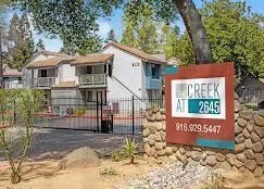 Apartment complex entrance sign reading “The Creek at 2645,” with buildings and trees in the background.