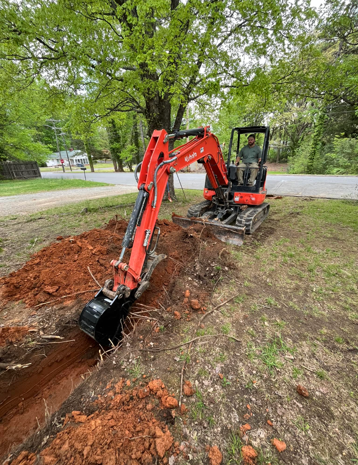 A red excavator is digging a hole in the ground.