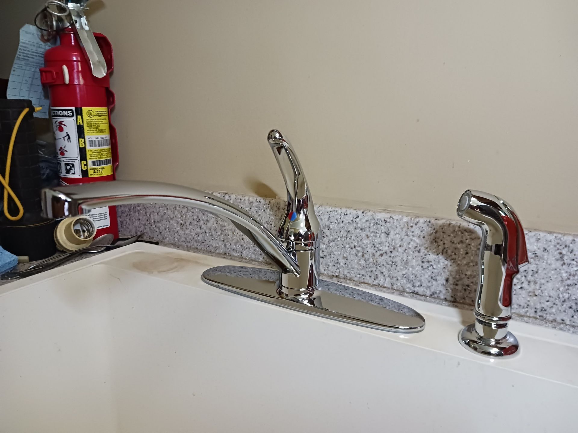A kitchen sink with a fire extinguisher in the background