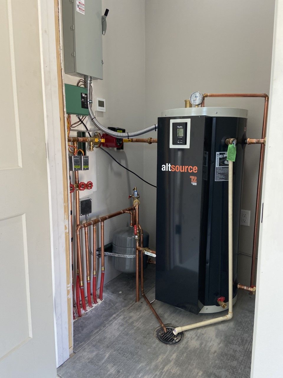 Interior mechanical room with a black water heater, copper pipes, and control panel.
