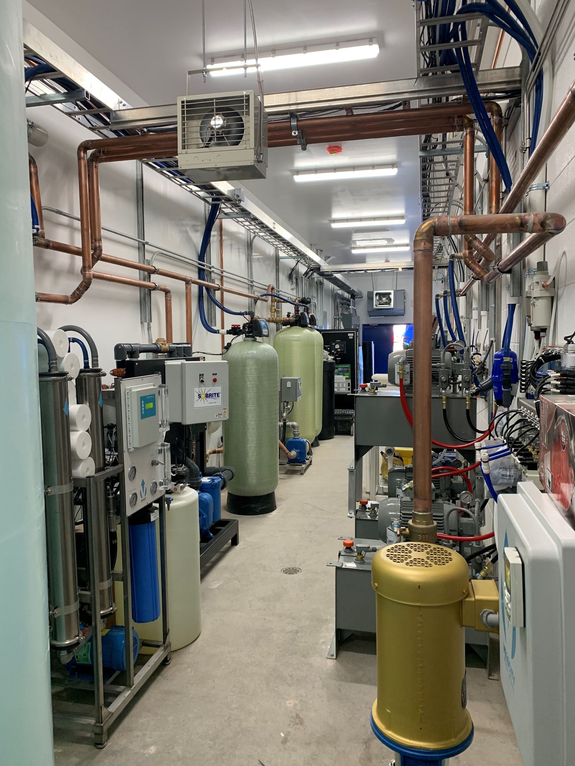 Interior view of a utility room with water treatment equipment, copper pipes, and tanks.
