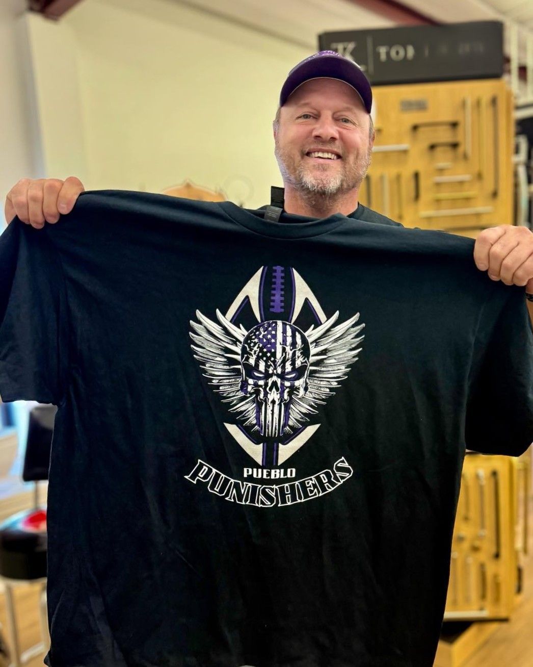 Man holding up a black t-shirt with a skull and wings design. The shirt says 