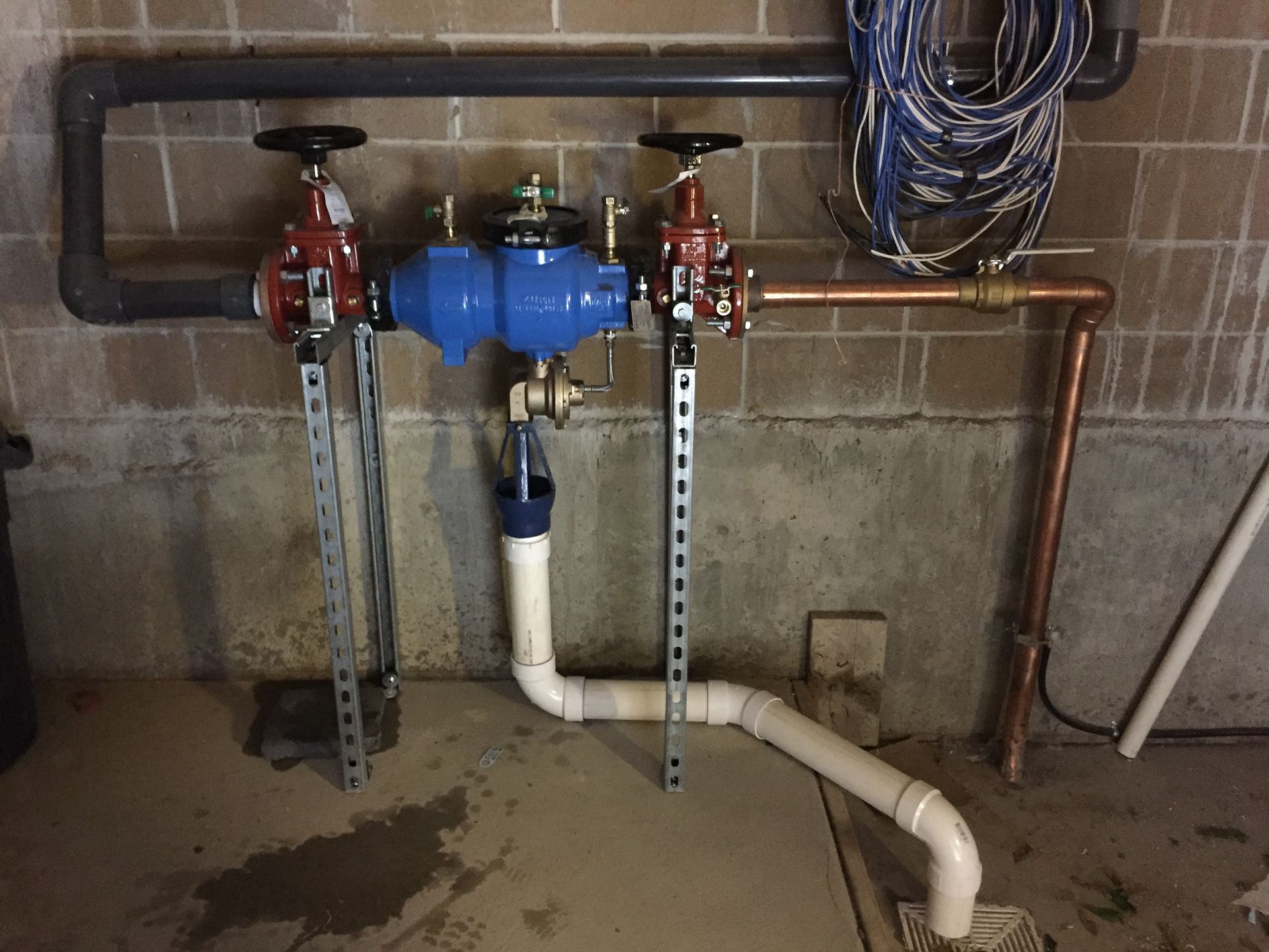 Plumbing system with blue water meter, valves, and pipes, against a brick wall in a basement setting.