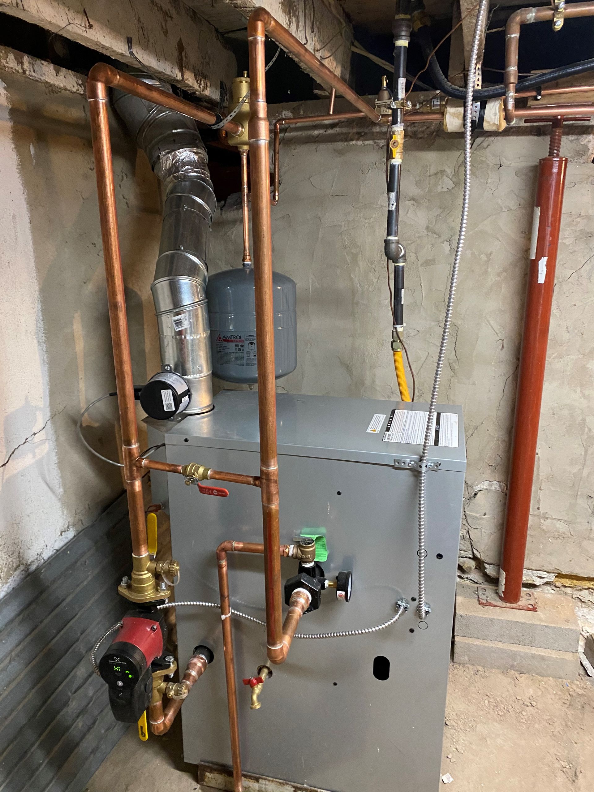 Copper pipes and plumbing fixtures attached to a gray furnace in a basement.
