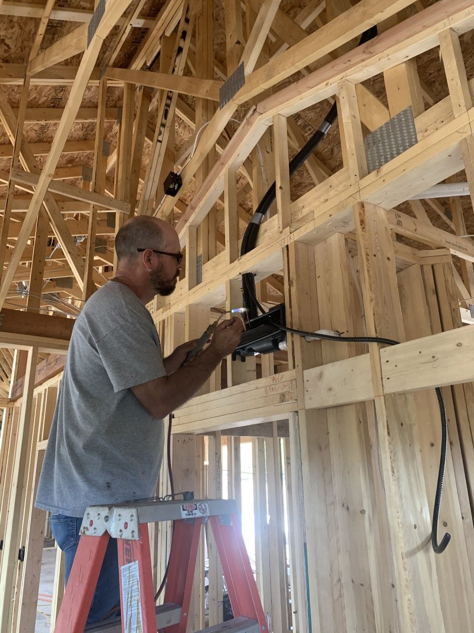 Man on ladder installing electrical wiring in a new home under construction.