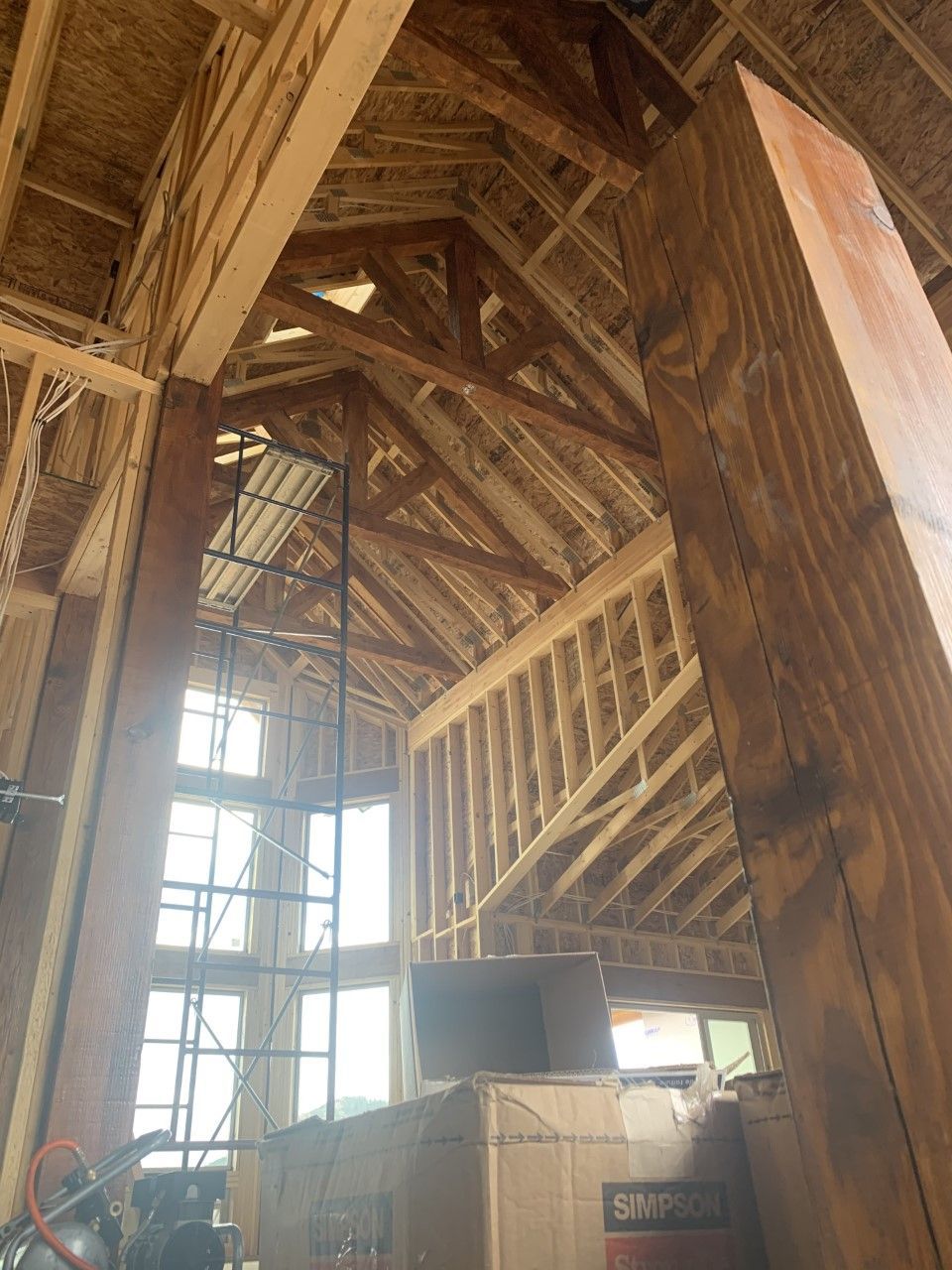 Interior view of a house under construction. Wood framing of walls, roof, and beams. Tall windows.