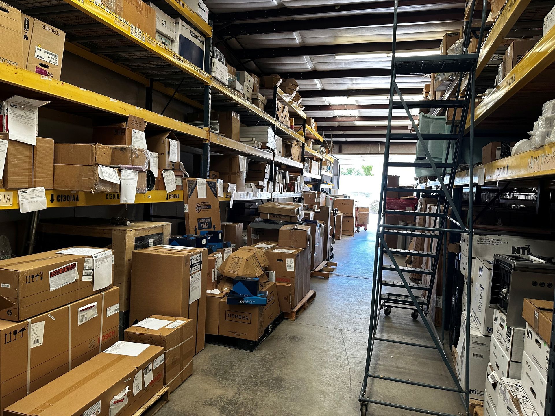 Warehouse aisle with boxes on shelves and floor, ladder in the center.