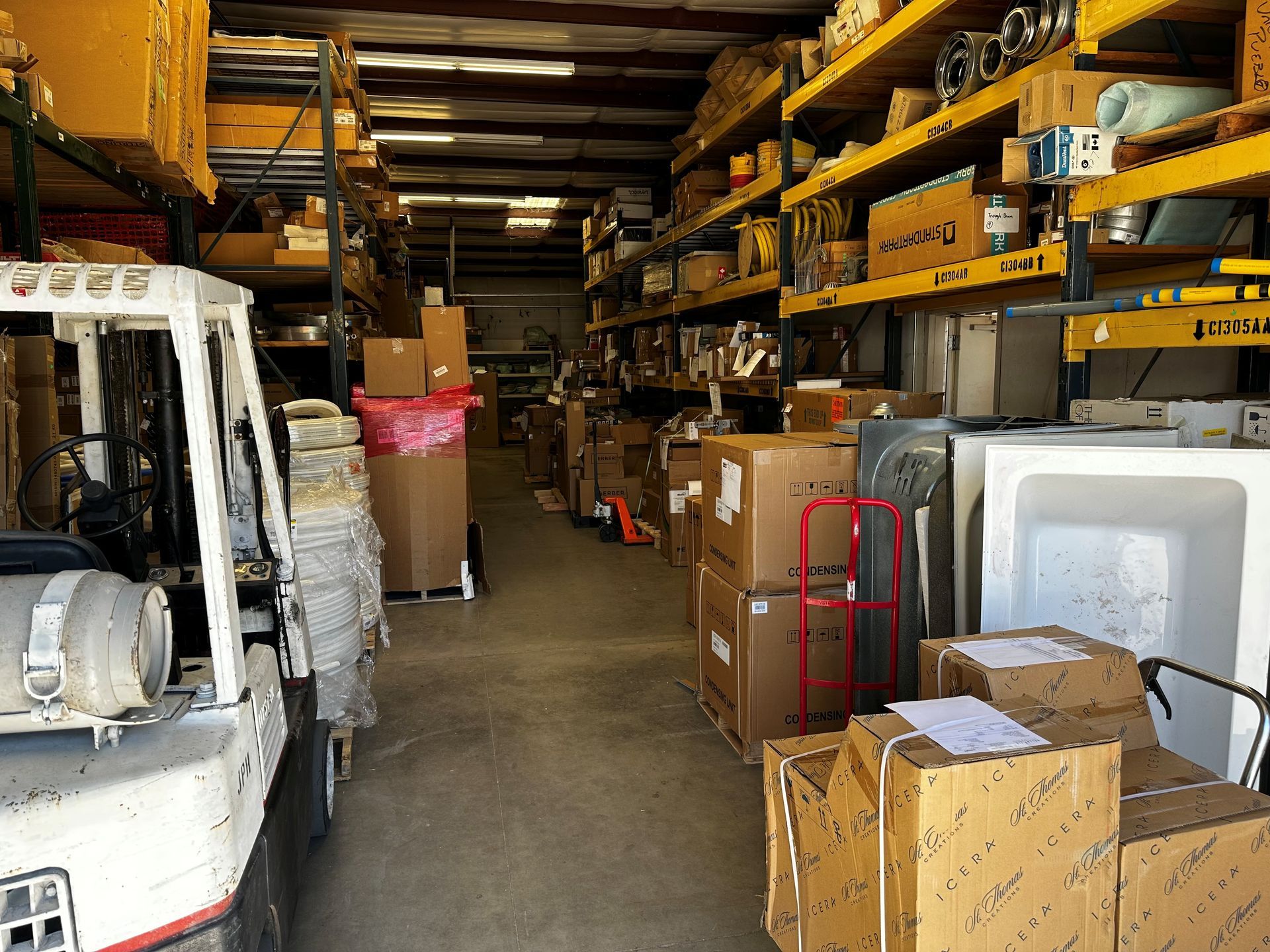 Warehouse interior with packed shelves and a forklift. Boxes, supplies, and a bathtub are visible.