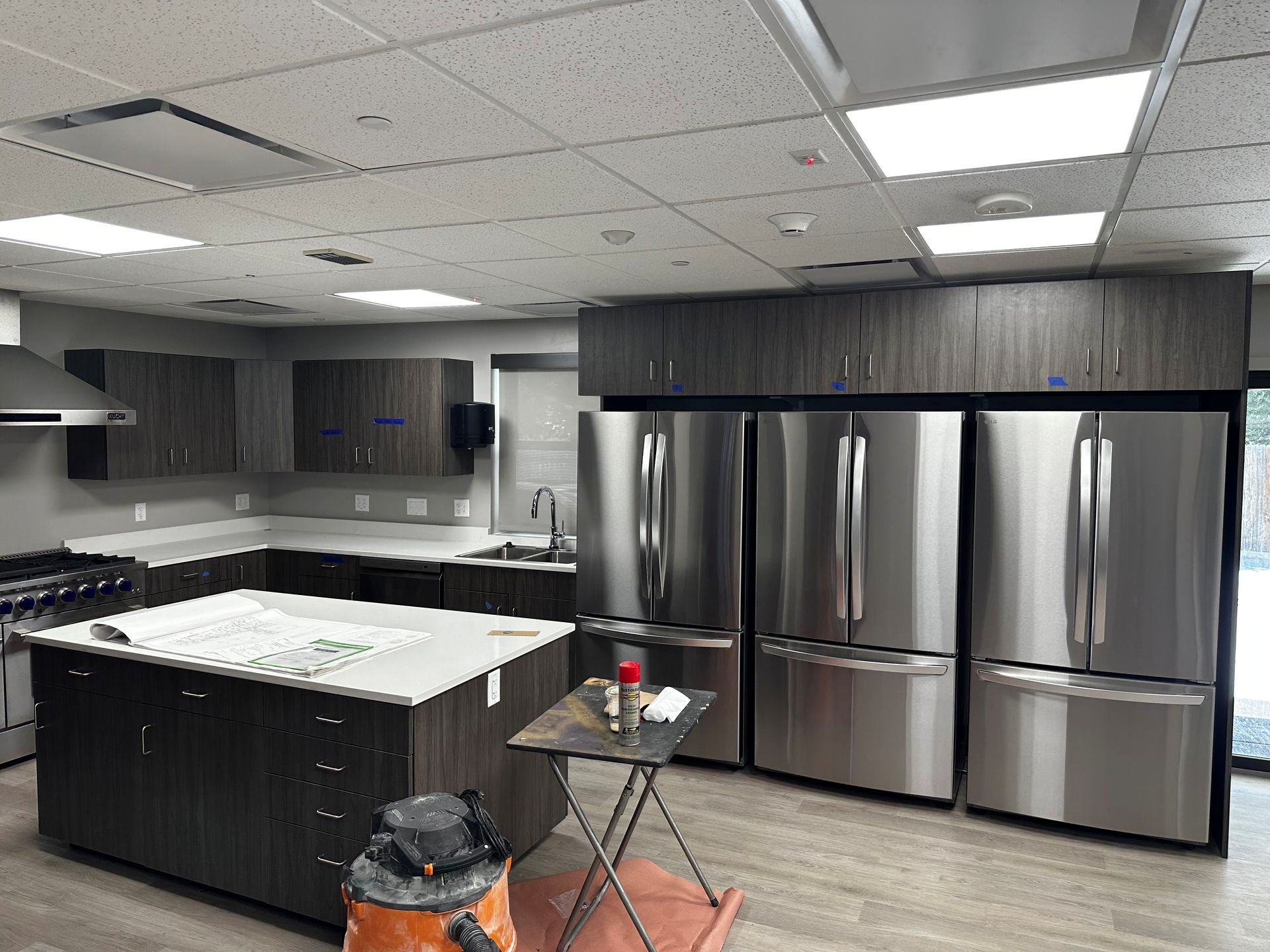 Kitchen with dark cabinets, stainless steel appliances, island, and white countertops.