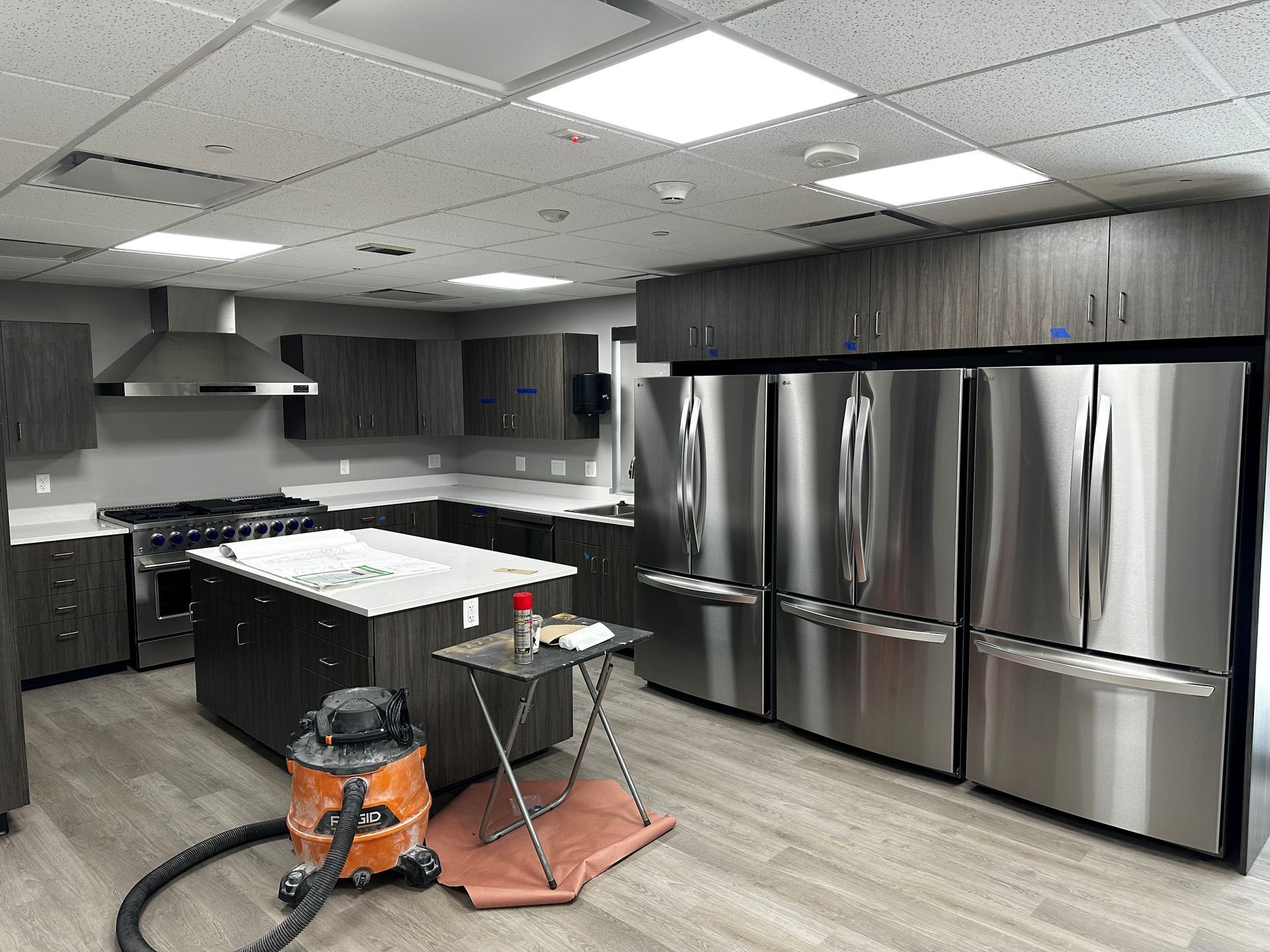 A modern kitchen with dark cabinetry, stainless steel appliances, and an island. A vacuum cleaner is present.