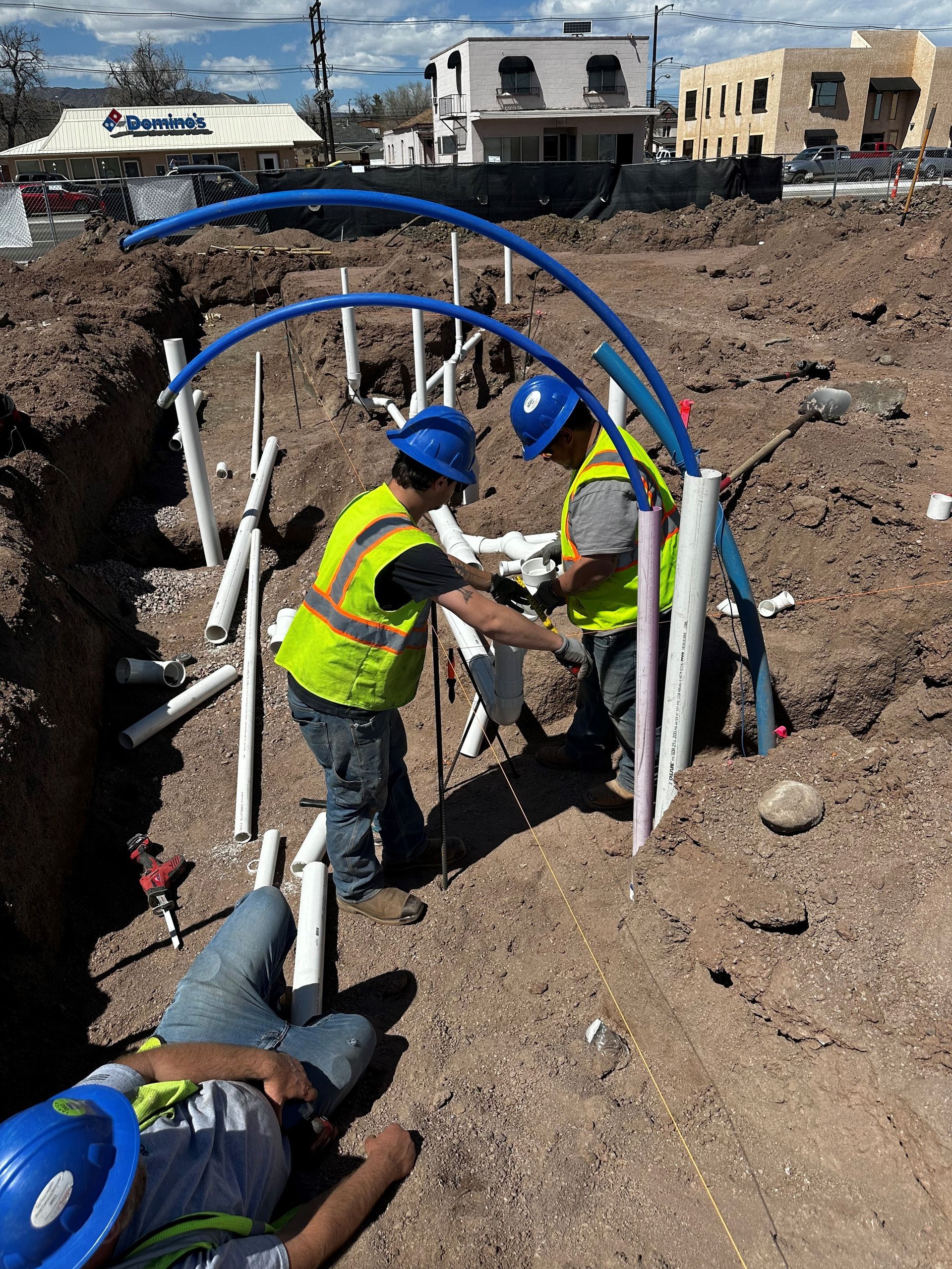 Construction workers install pipes in a trench; one rests nearby.