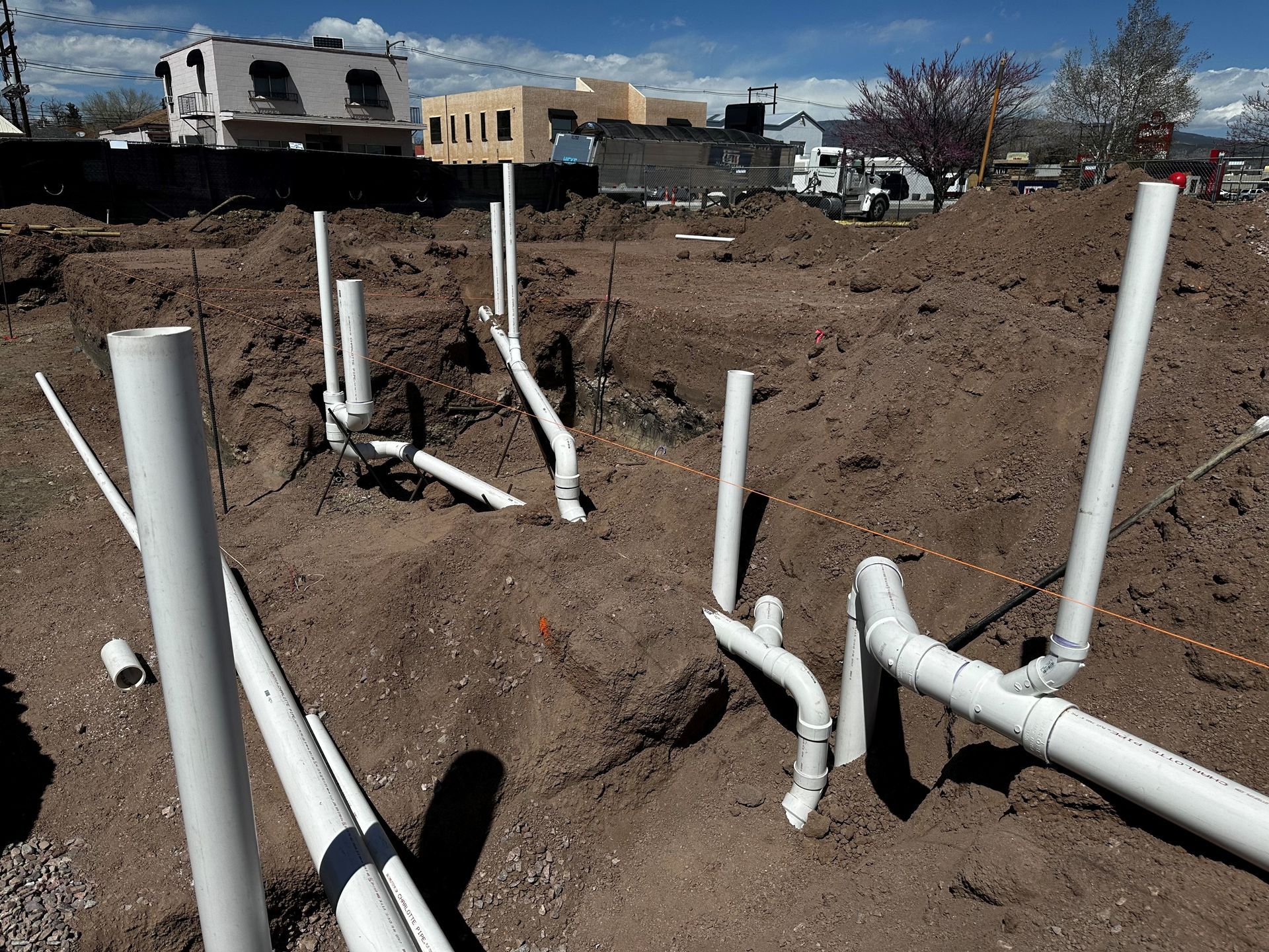 White plumbing pipes in brown dirt at a construction site, a blue sky in the background.