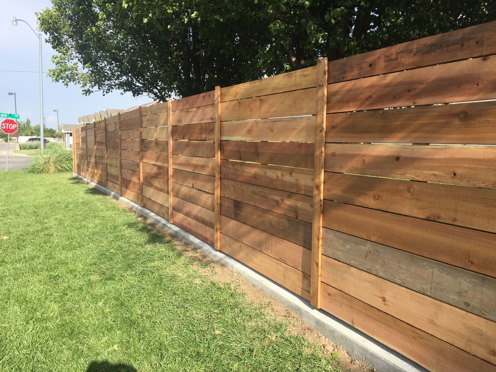 A horizontal cedar wood slat fence installed on a concrete foundation next to a green lawn.