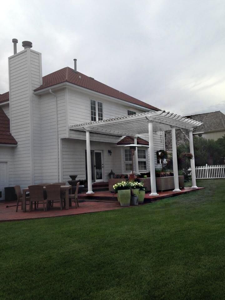 A white two-story house with a white pergola covering a red patio, outdoor furniture, and a grassy backyard.