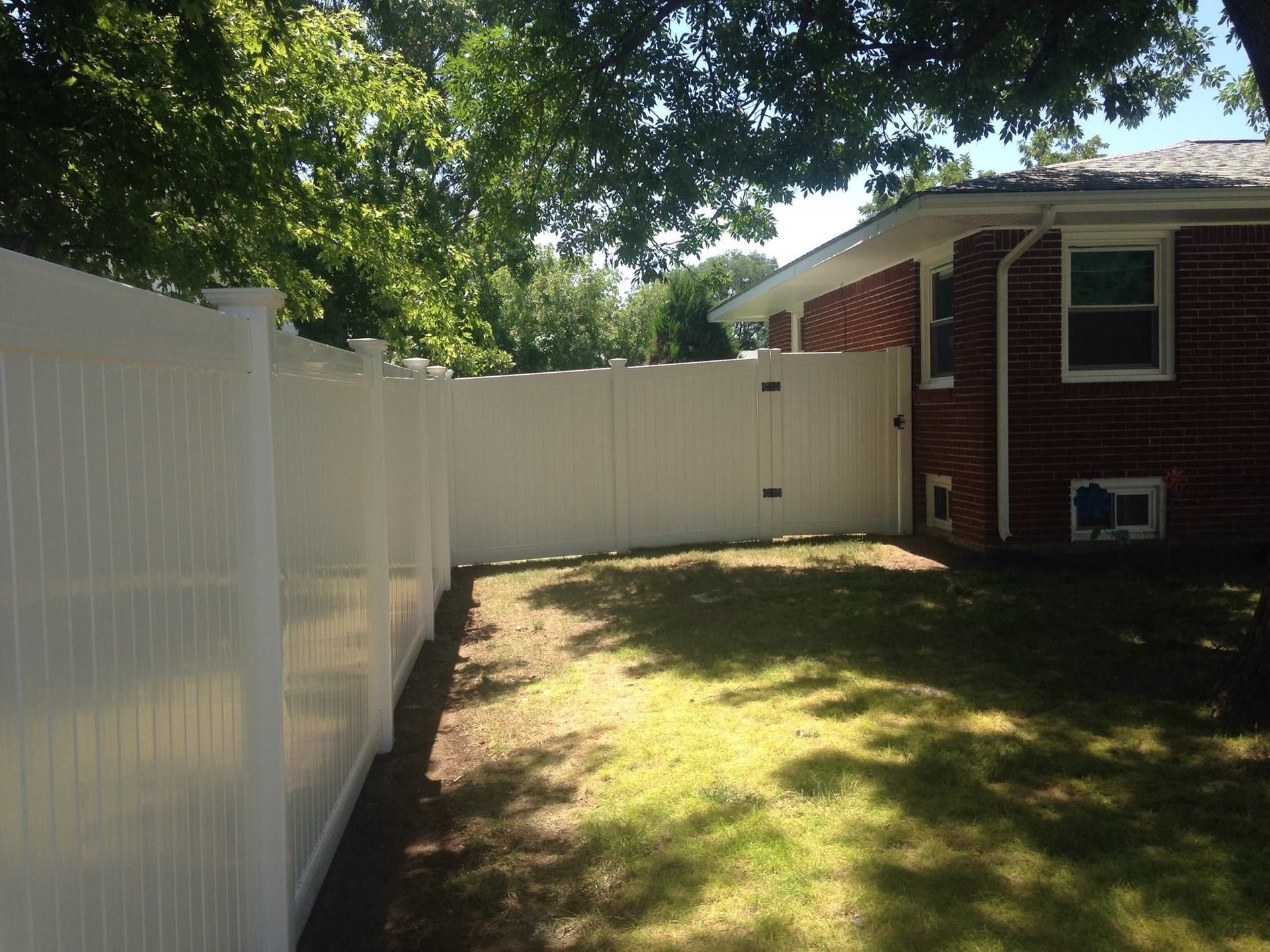 A tall, white vinyl privacy fence encloses a backyard next to the side of a red brick house.