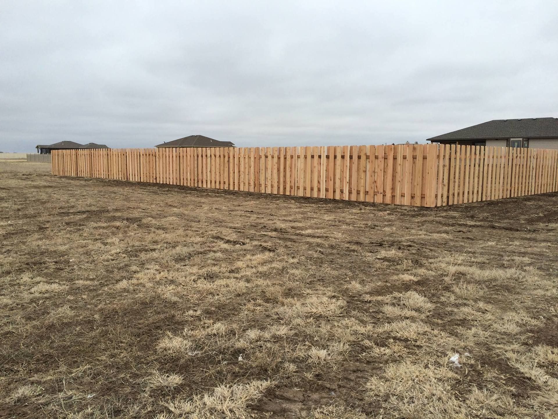 A wooden privacy fence surrounds a vacant lot under a cloudy sky.