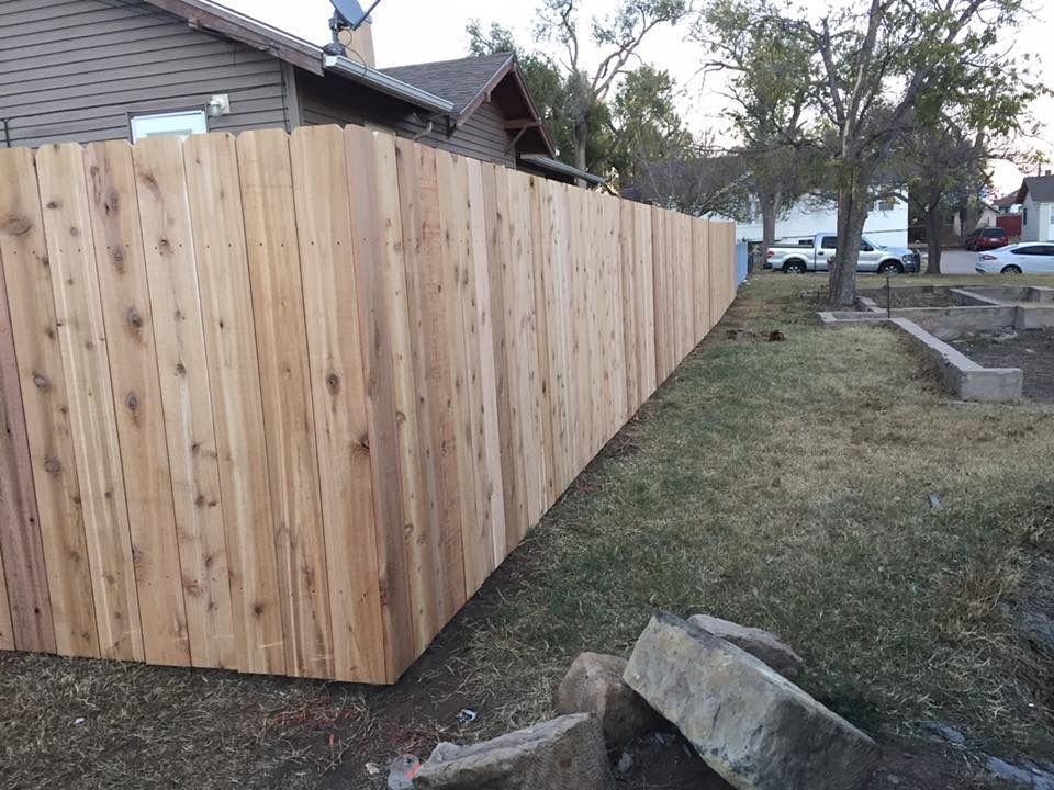 A newly built, light-wood privacy fence runs along the side of a yard near a house.