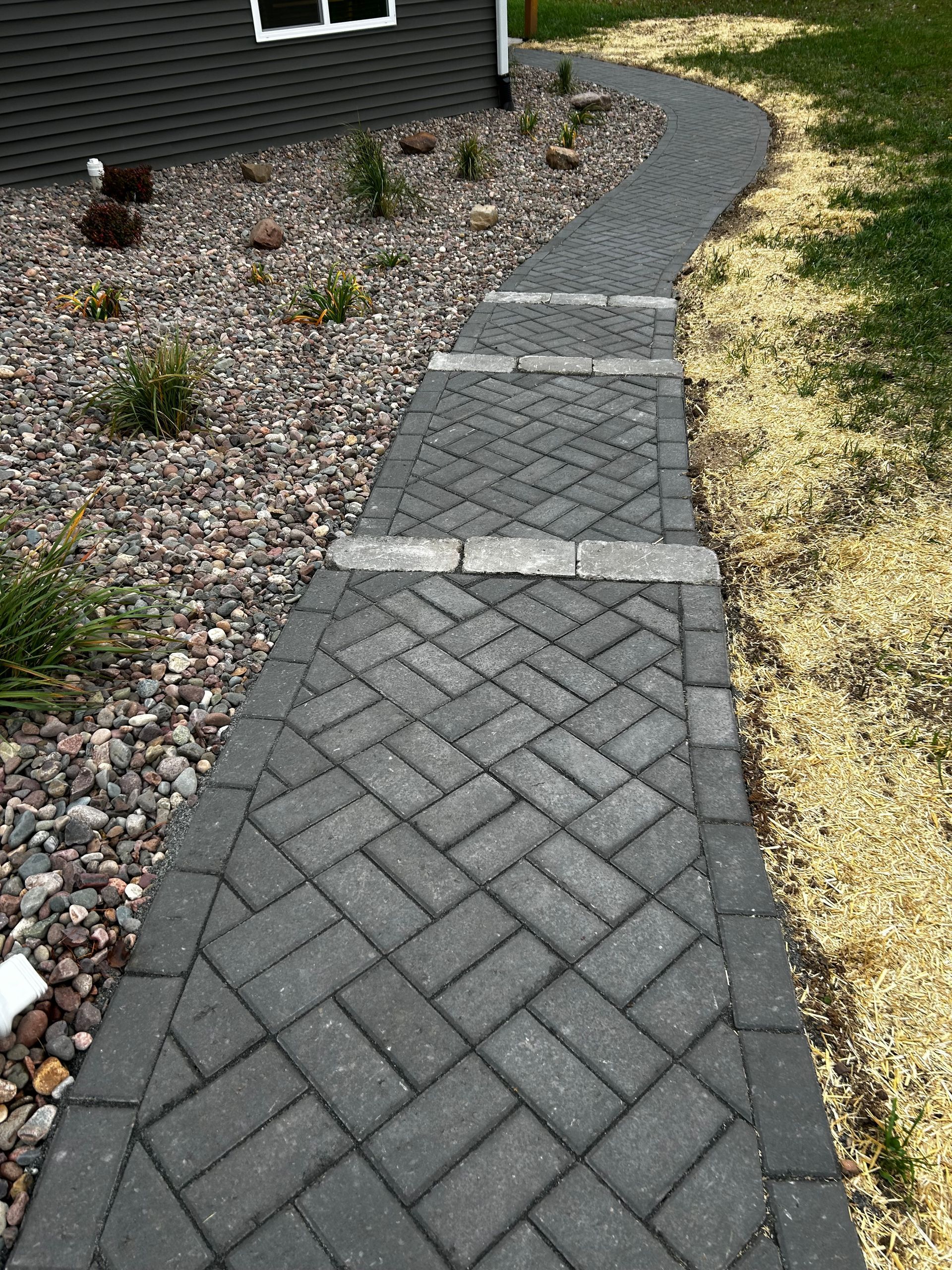 A brick walkway leading to a house with a herringbone pattern.