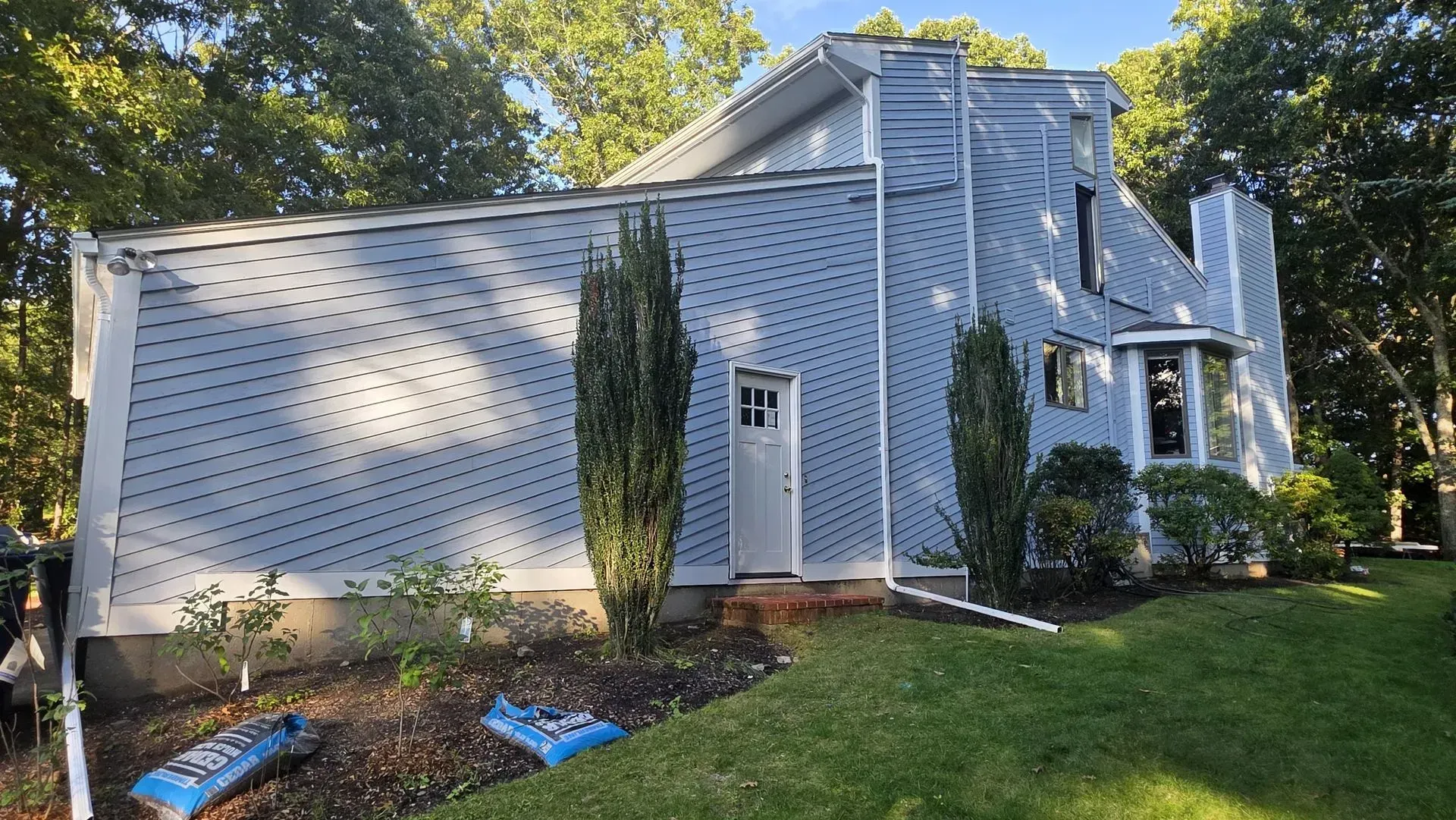 Gray two-story house with white trim and blue shutters, front lawn, and a small landscaped garden.