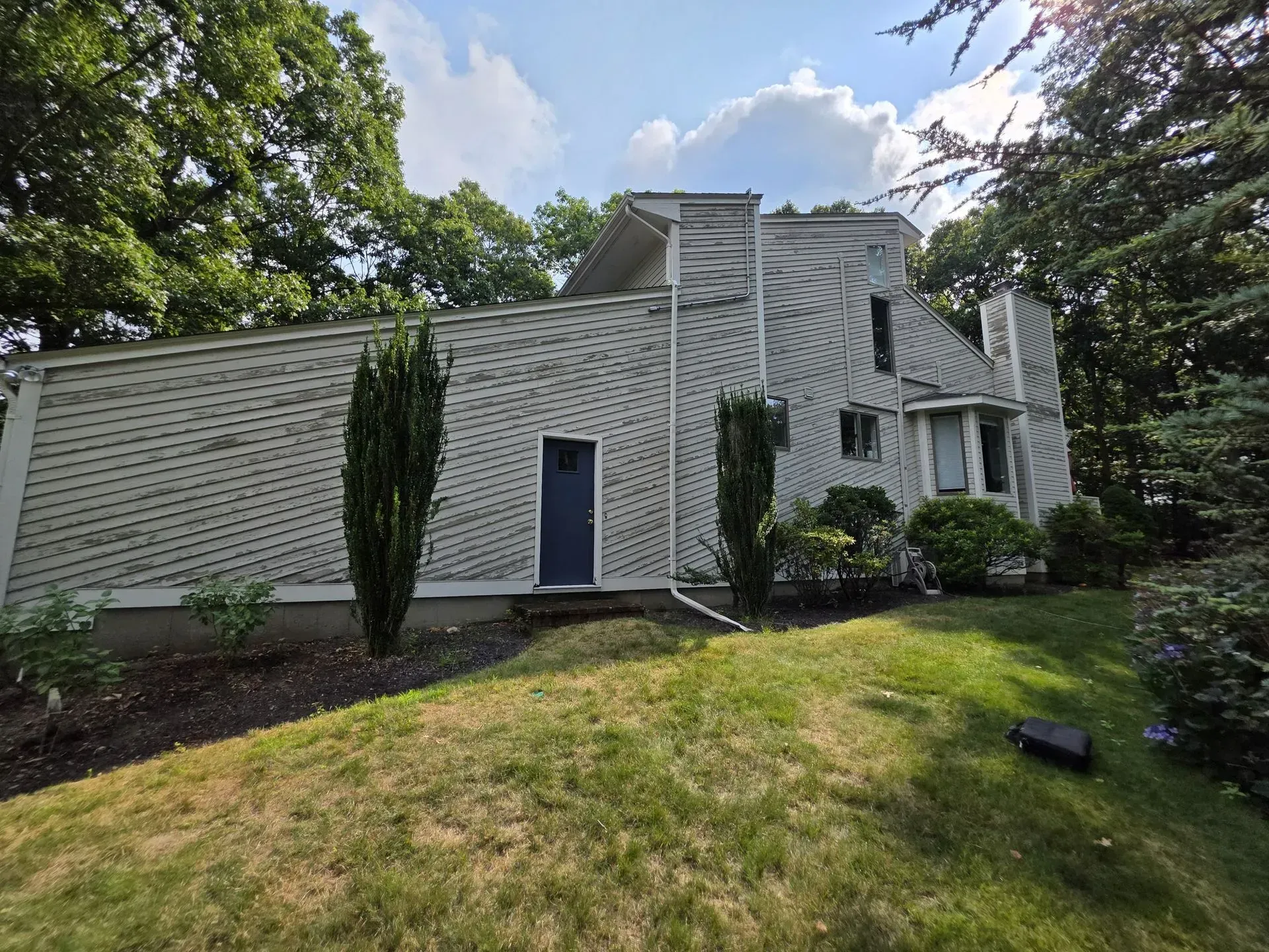 White two-story house with gray siding, dark doors, and trees in a grassy yard.