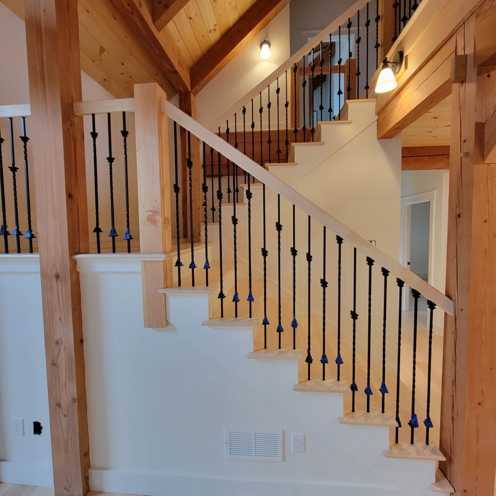 Wooden staircase with black iron balusters in a bright rustic interior cabin.