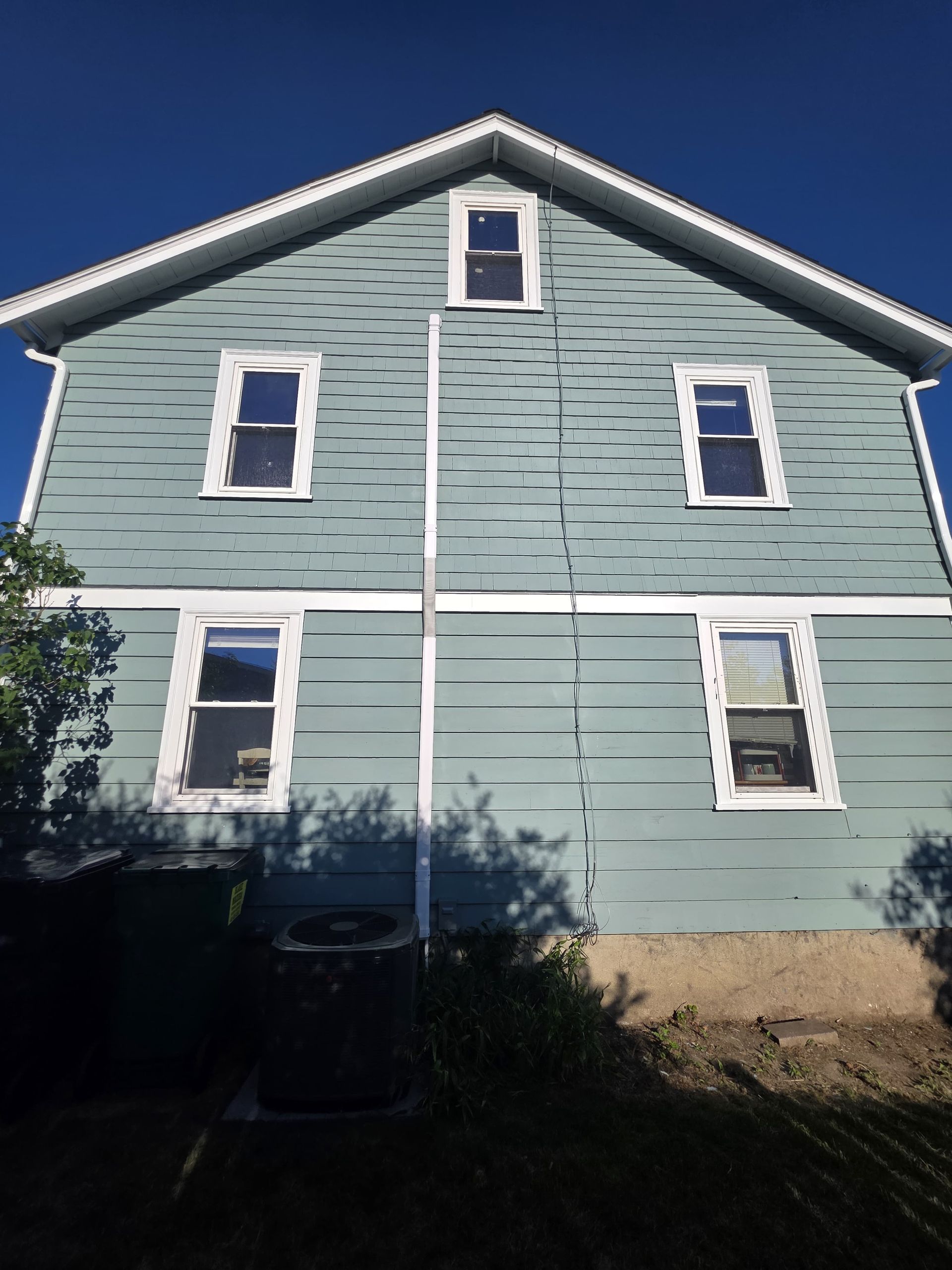 Light blue two-story house with white trim and a steep gabled roof against a clear sky