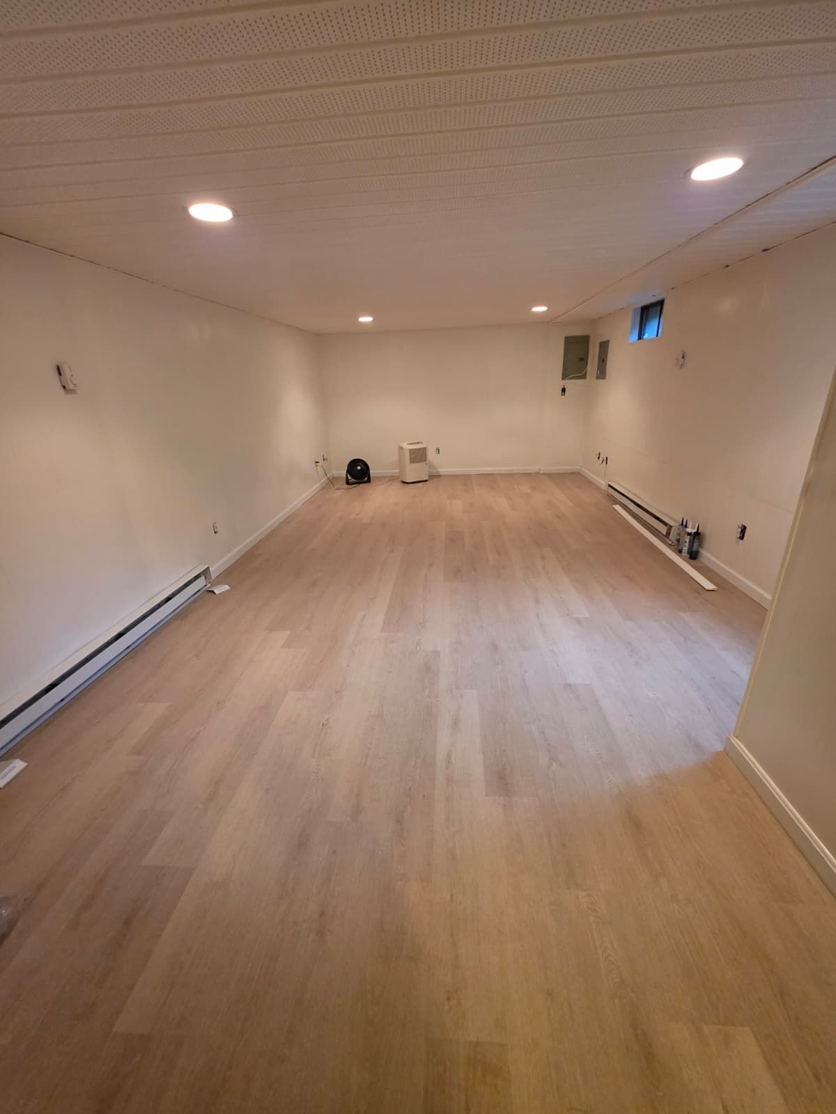 Empty white room with light wood floor, recessed ceiling lights, and small wall fixtures.